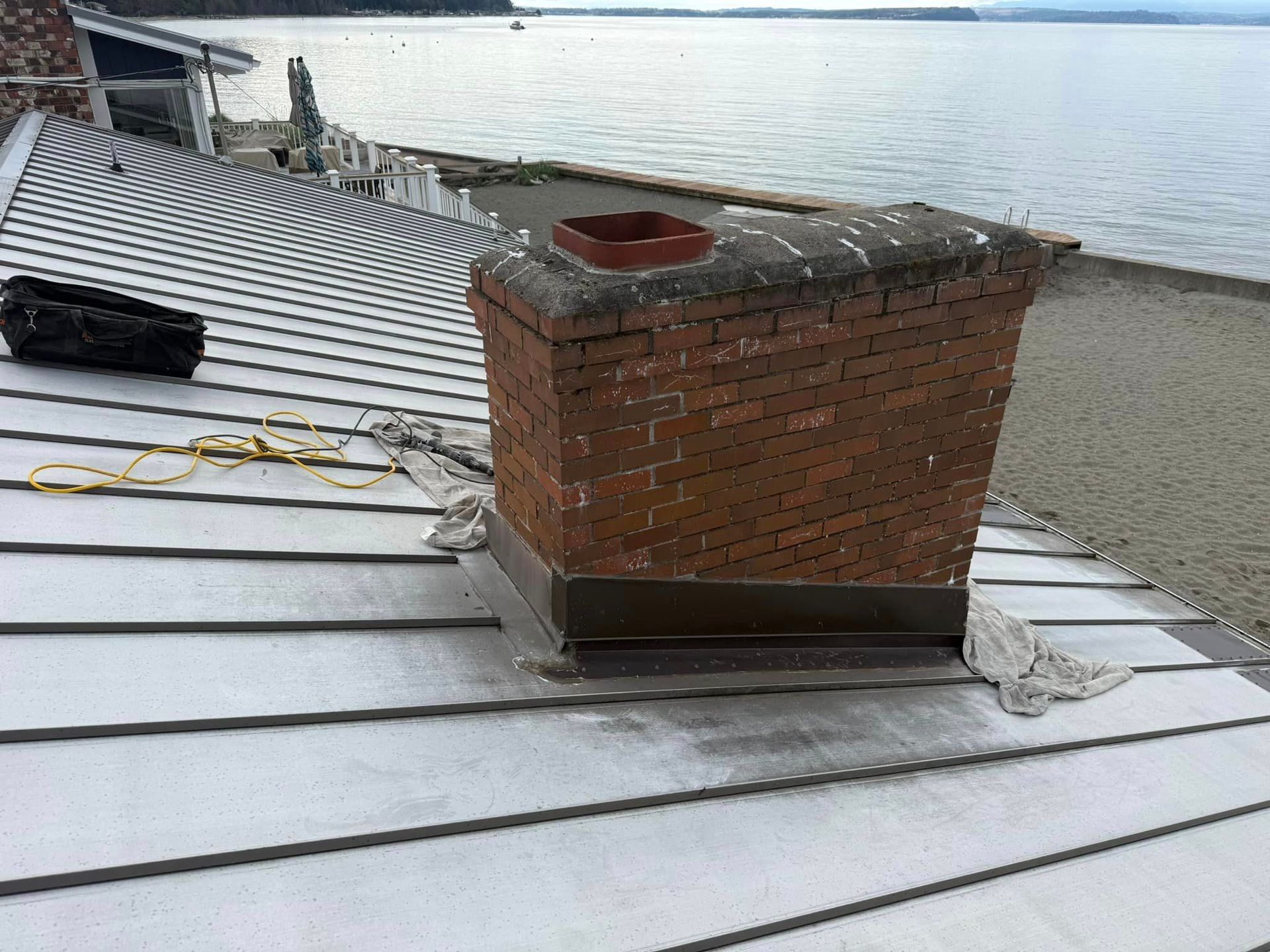 A brick chimney is sitting on top of a metal roof next to a body of water.