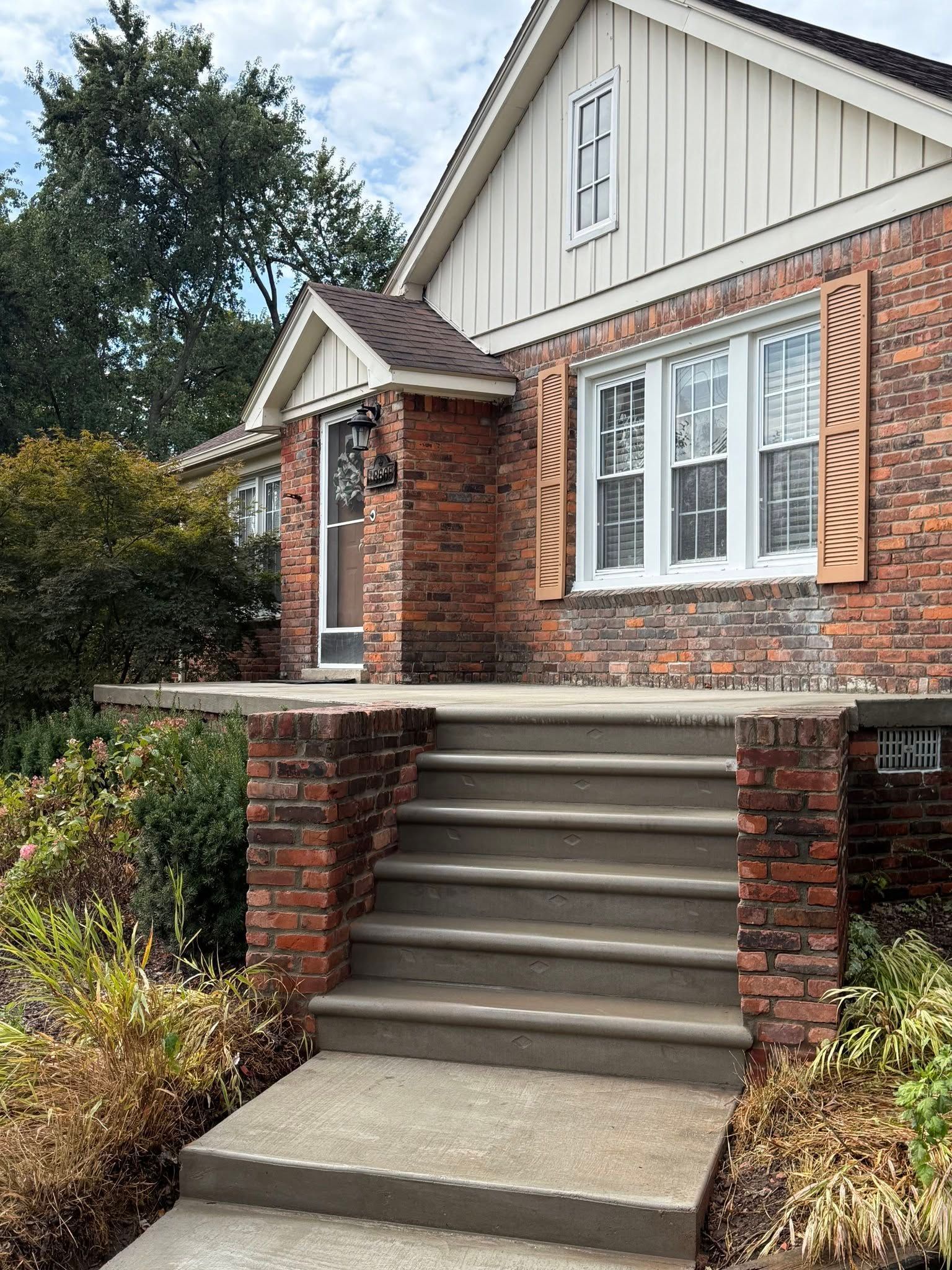 Brick house front entrance with concrete steps, white windows, and a landscaped walkway