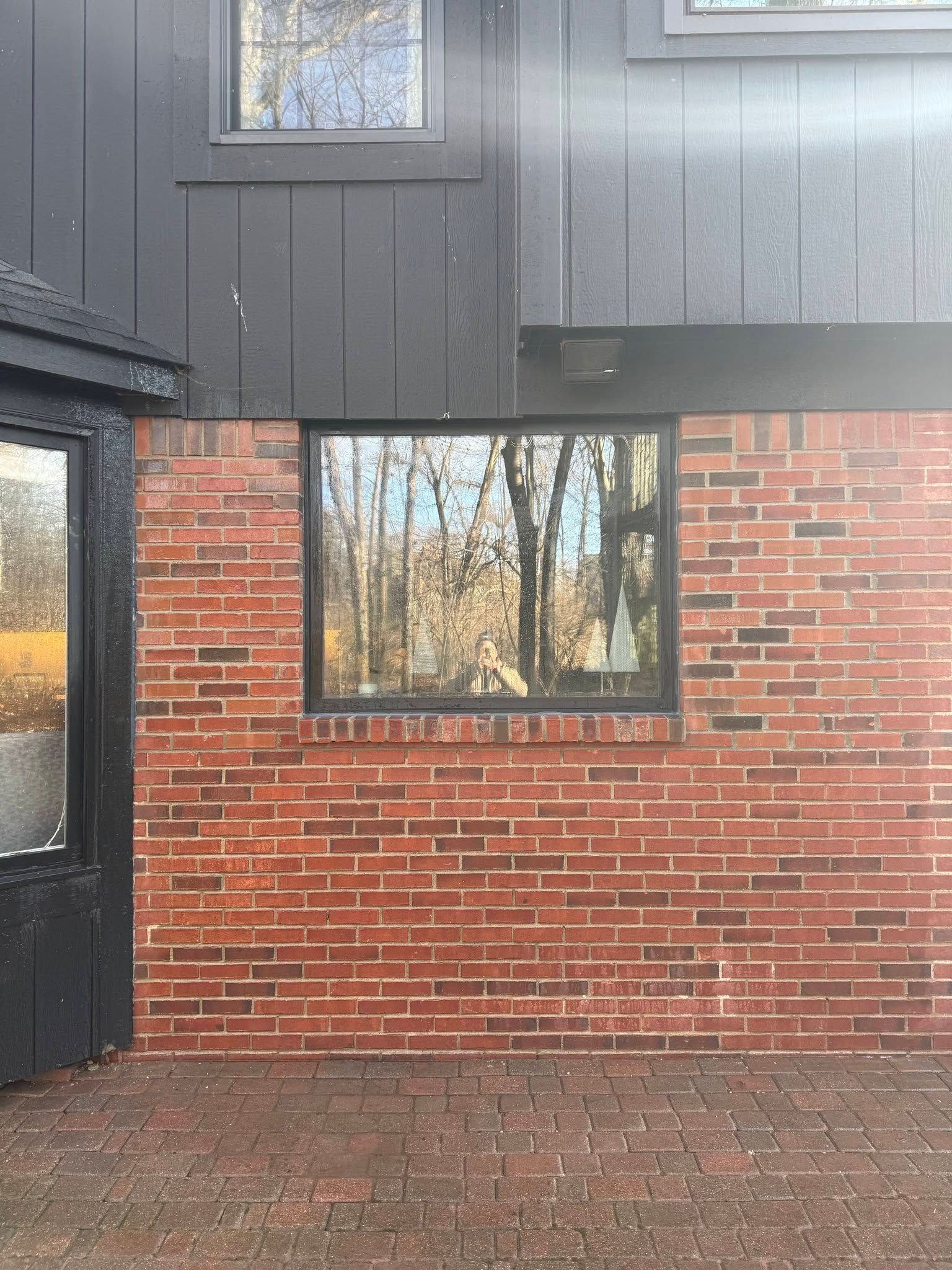 Red brick and dark gray building exterior with windows and a paved walkway below.