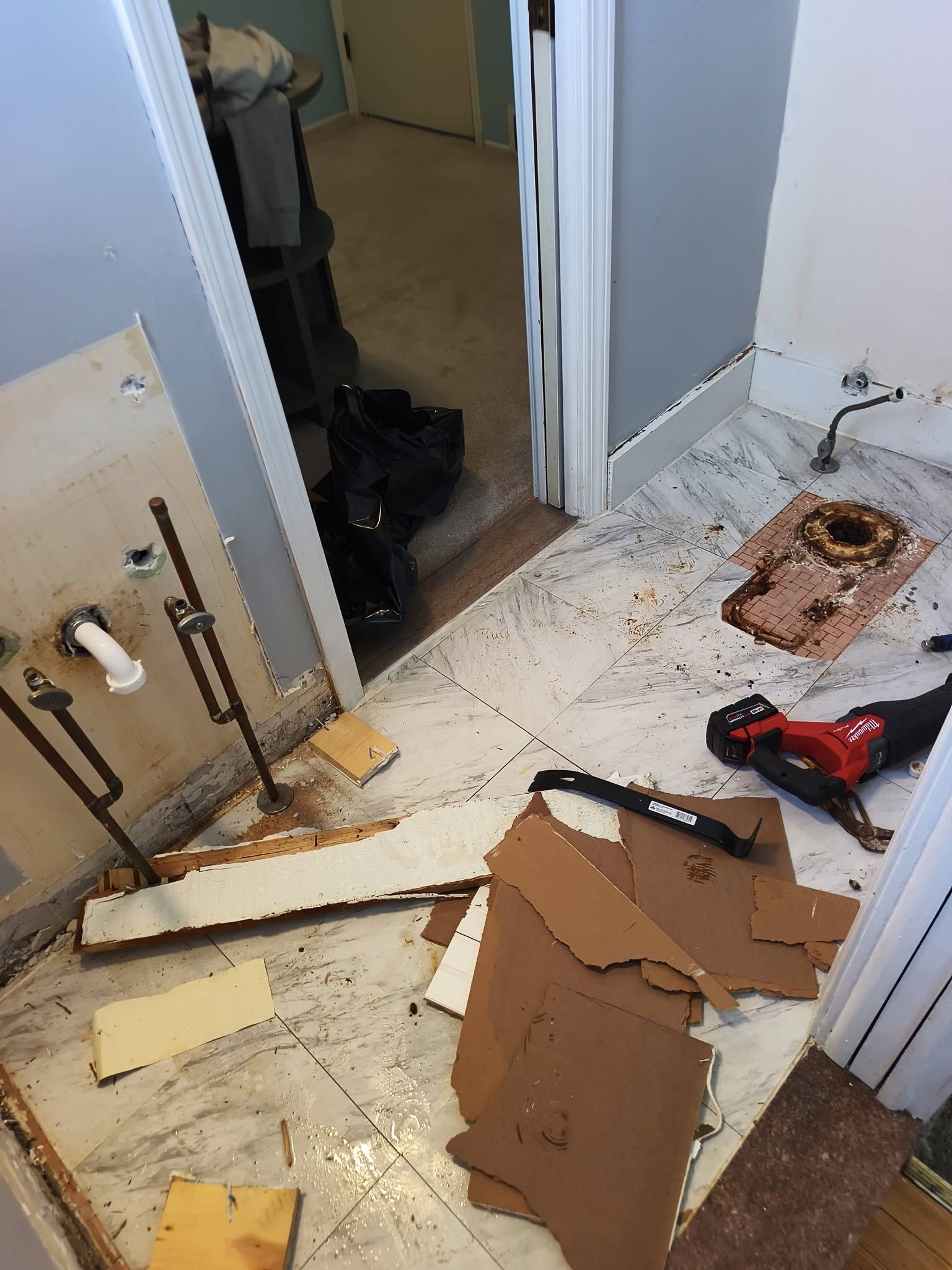 Damaged bathroom floor with debris, broken board, and a rusted fixture near a doorway