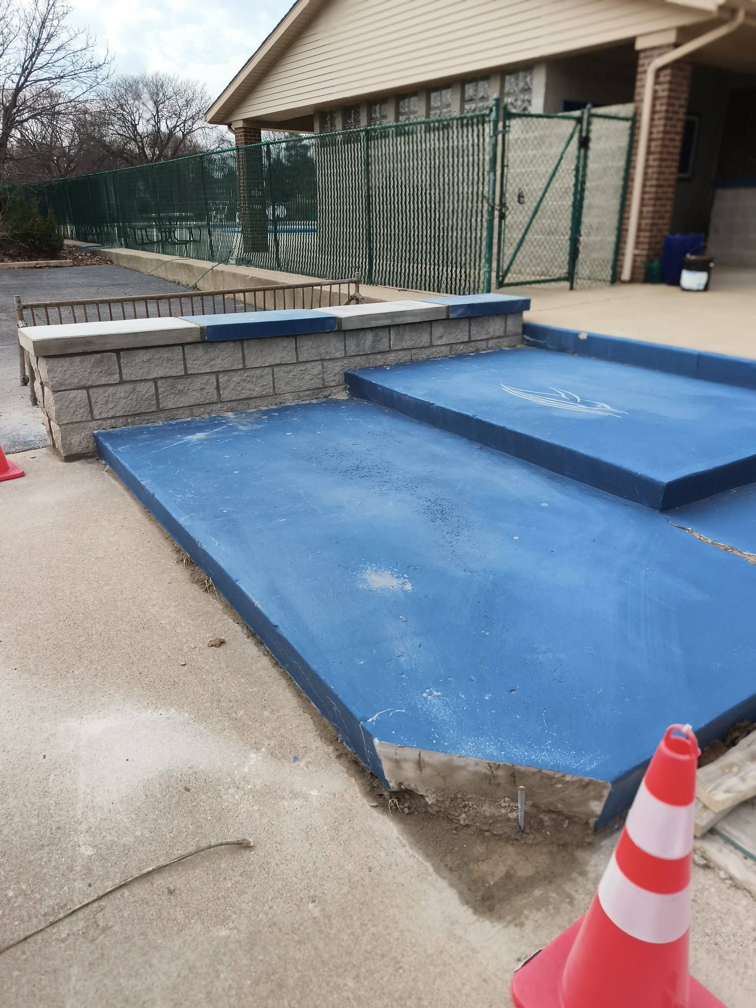 Blue accessibility ramp and steps beside a stone wall at a house, with a traffic cone in front.