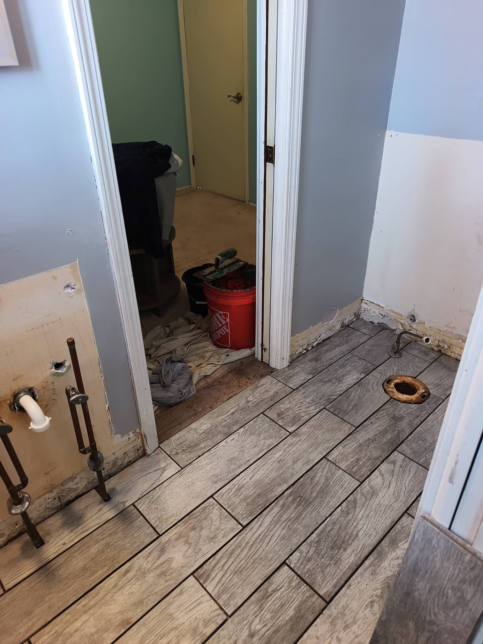 Narrow hallway with exposed floorboards, open doorway, and a red bucket in a damaged interior.