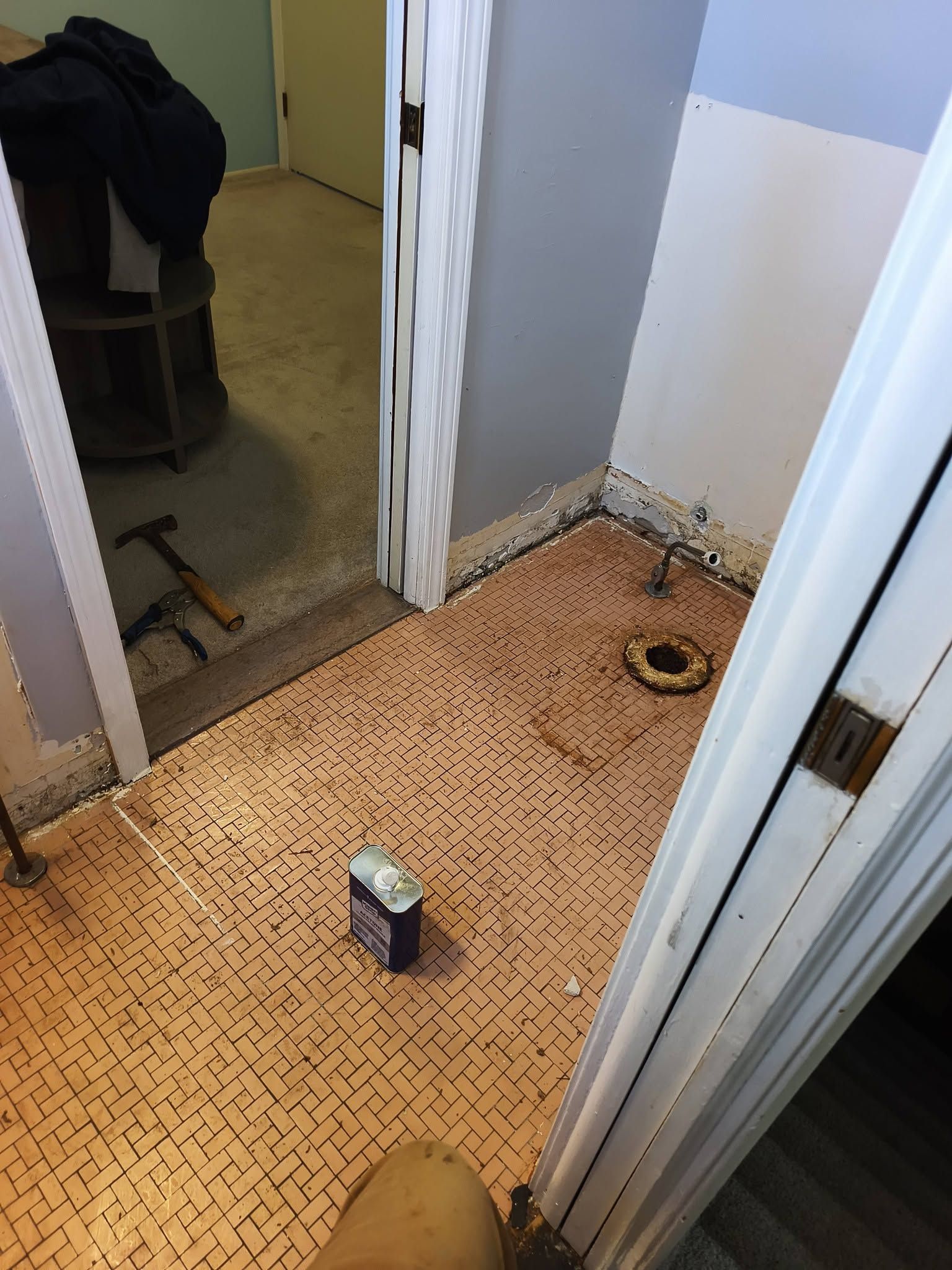Bathroom floor with removed toilet, exposed drain, and a cleaning bottle on tan tile.