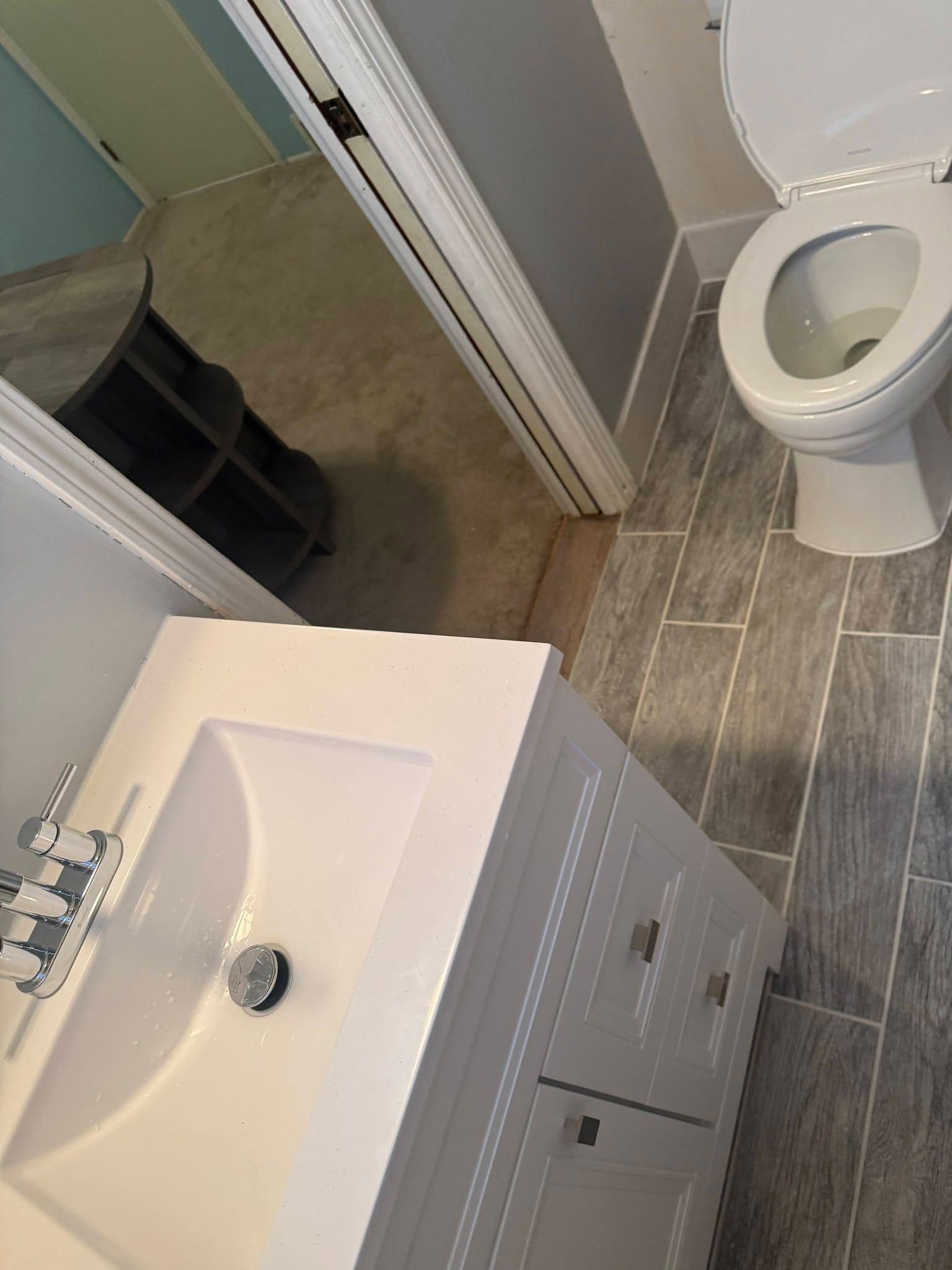 Small bathroom with sink vanity, toilet, and shower entrance, shown at an angle.