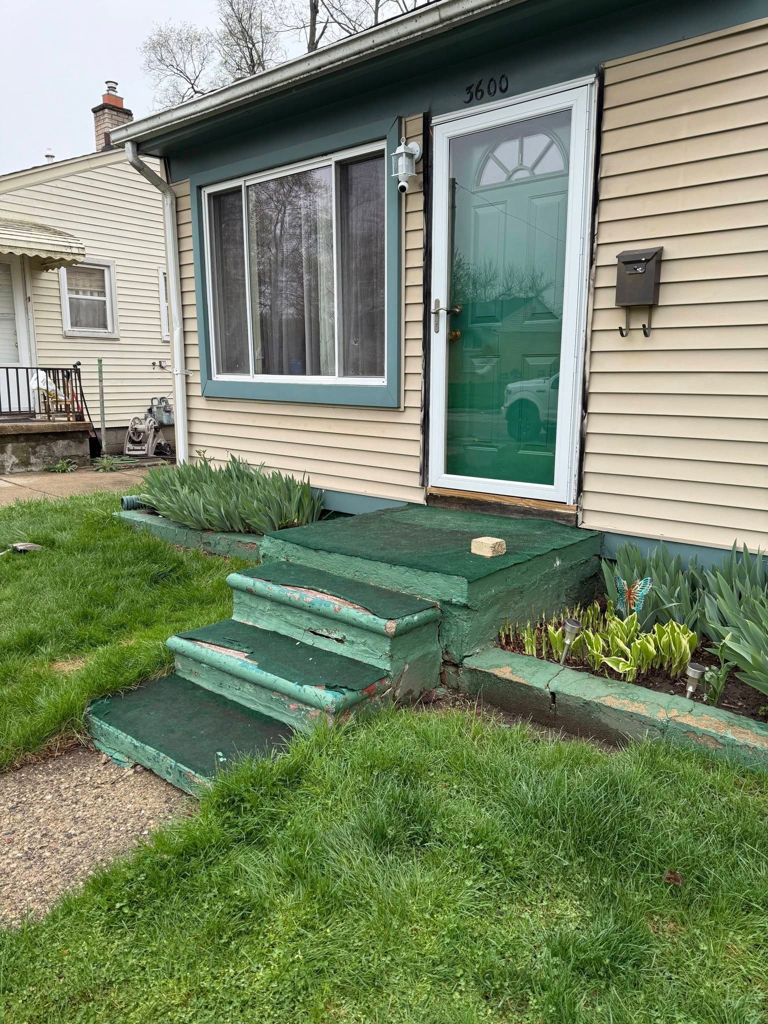 Green front porch steps and door of a beige house with small garden beds.