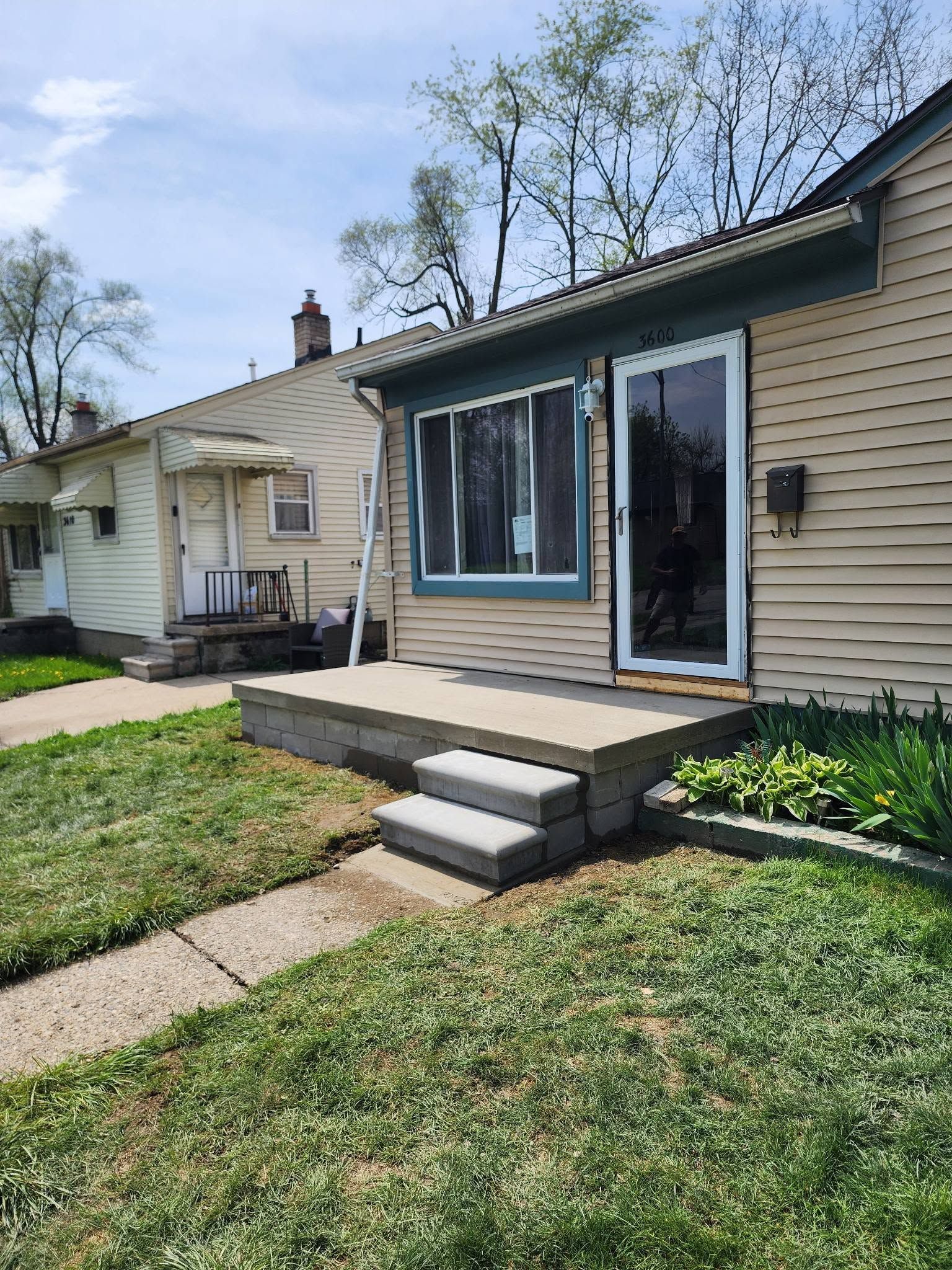 Backyard patio with steps, sliding glass door, and beige siding on a sunny day