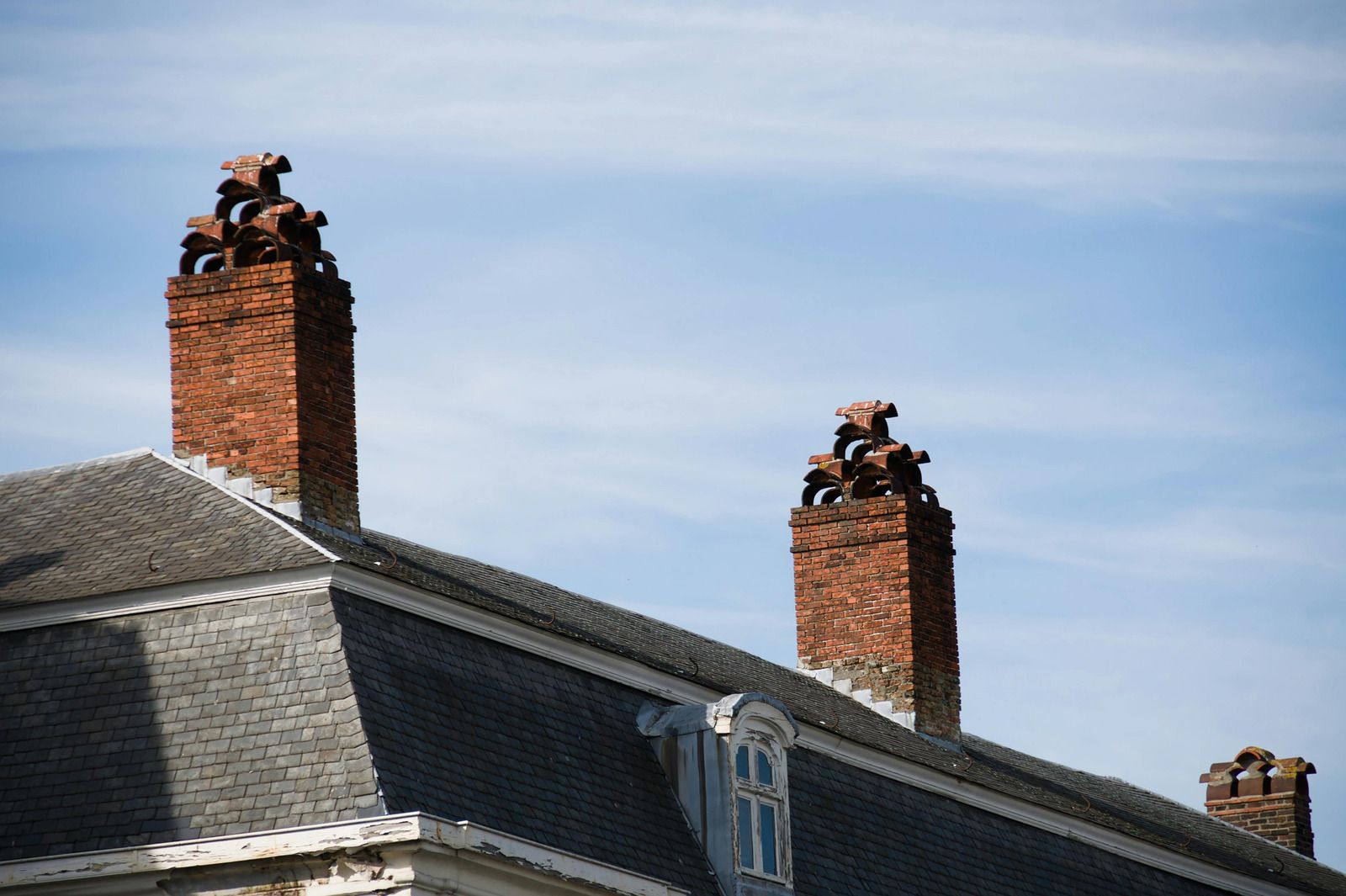 Slate roof with two red brick chimneys against a blue sky