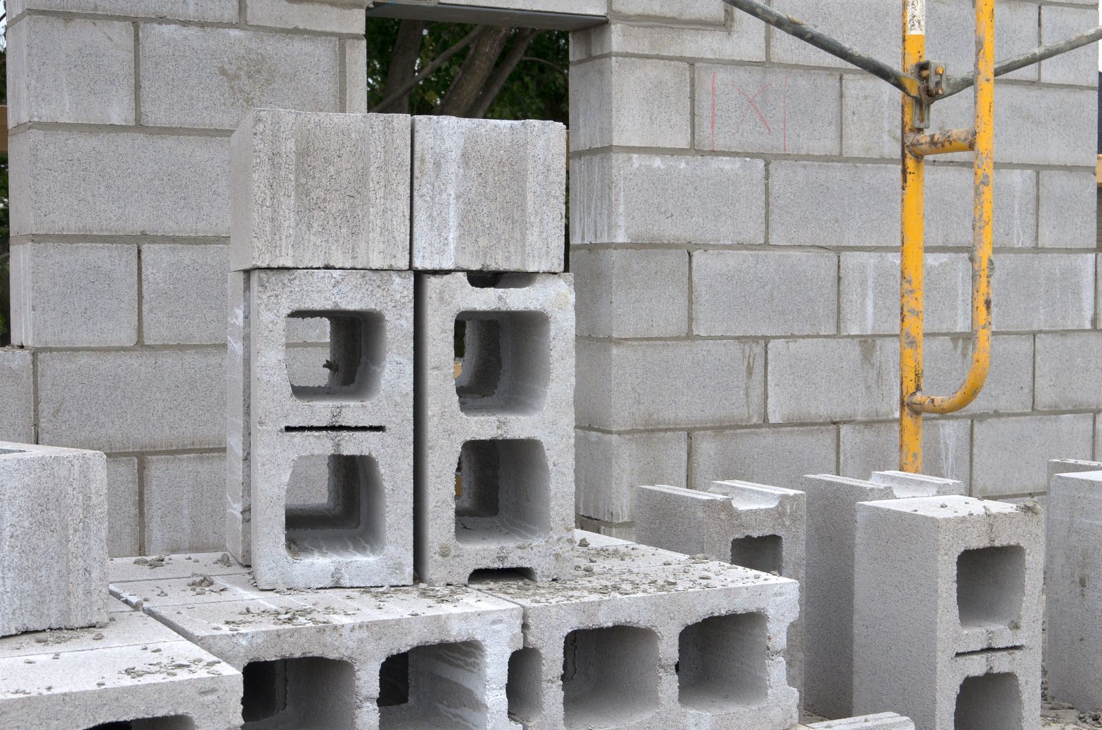 Stacked cinder blocks at a construction site beside a cinder block wall and ladder
