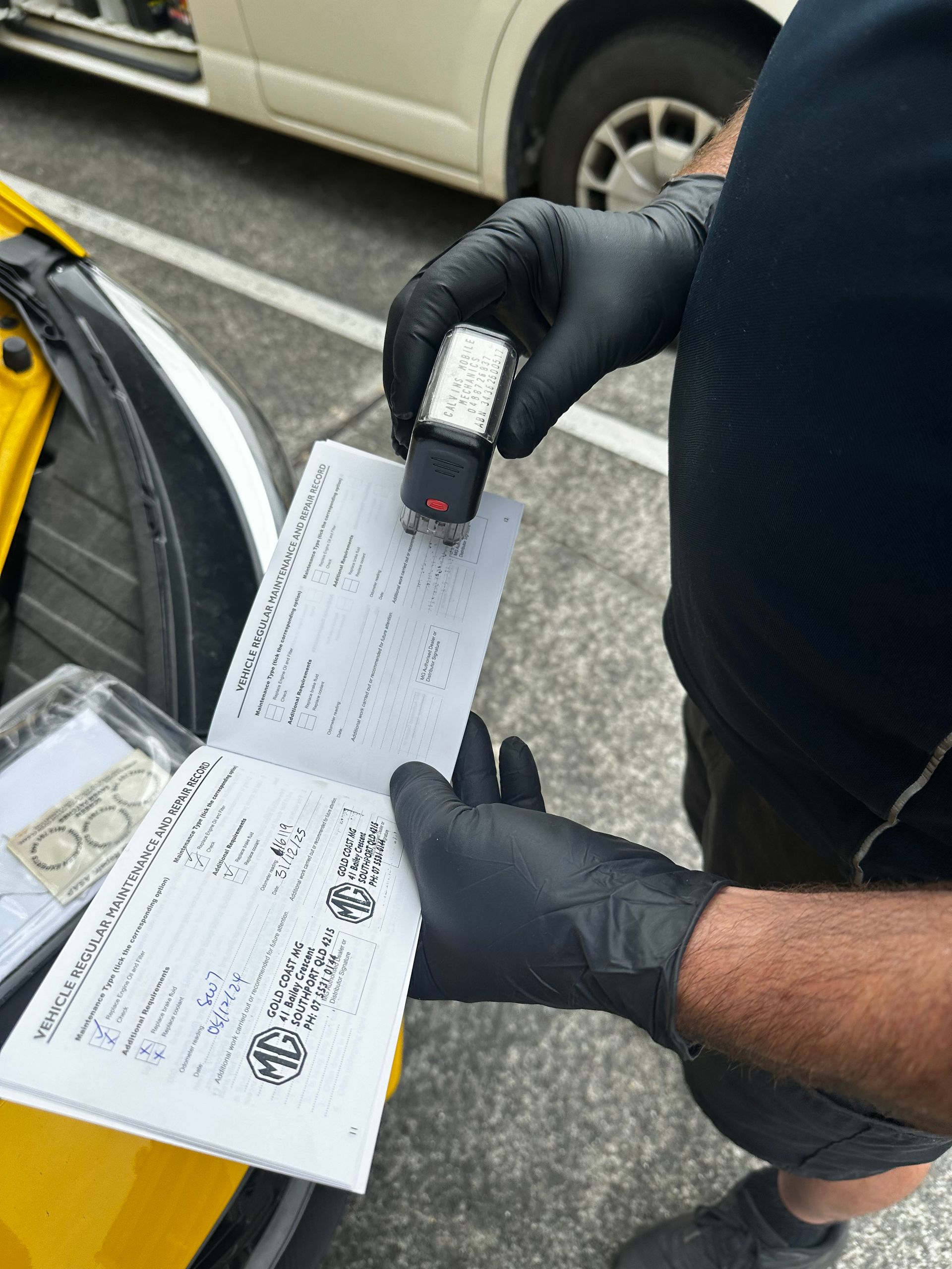 Gloved hands scan a document beside a car in a parking lot. — Calvin's Mobile Mechanics In Elanora, QLD