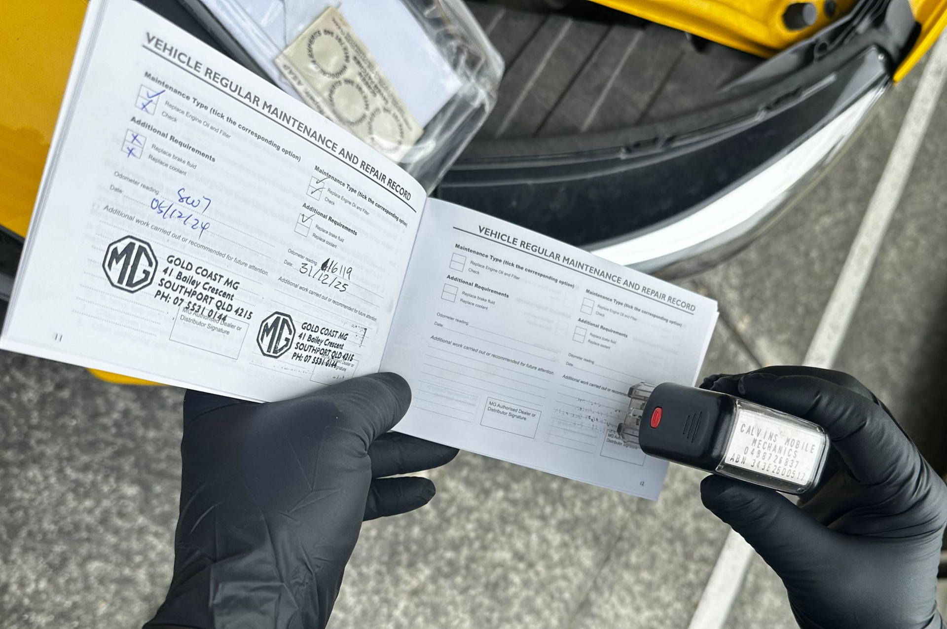 Gloved hands hold a form and a key fob beside a car trunk with paperwork and a yellow tool case — Calvin's Mobile Mechanics In Palm Beach, QLD