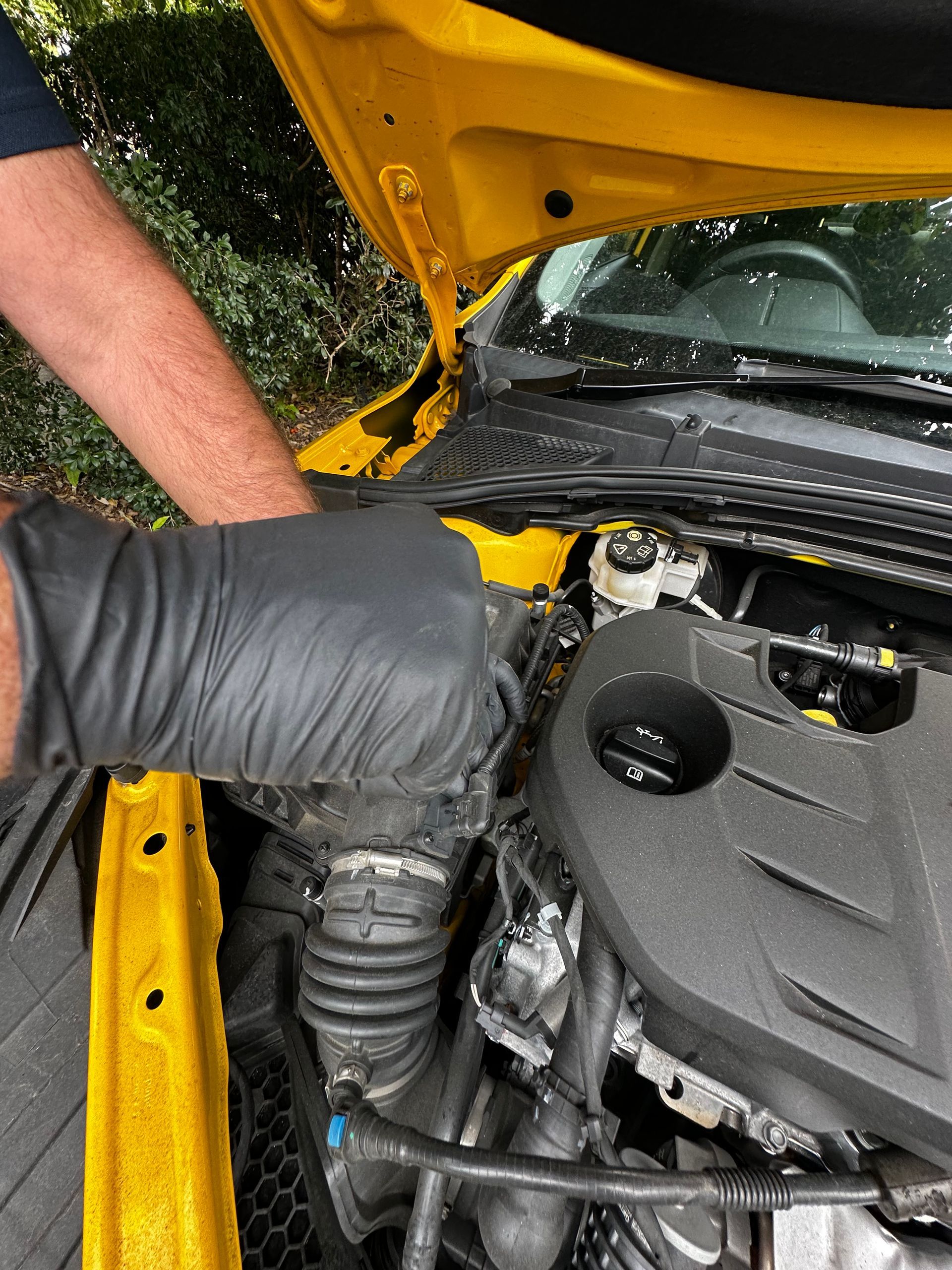 Gloved hand working inside the open hood of a yellow car engine bay — Calvin's Mobile Mechanics In Elanora, QLD