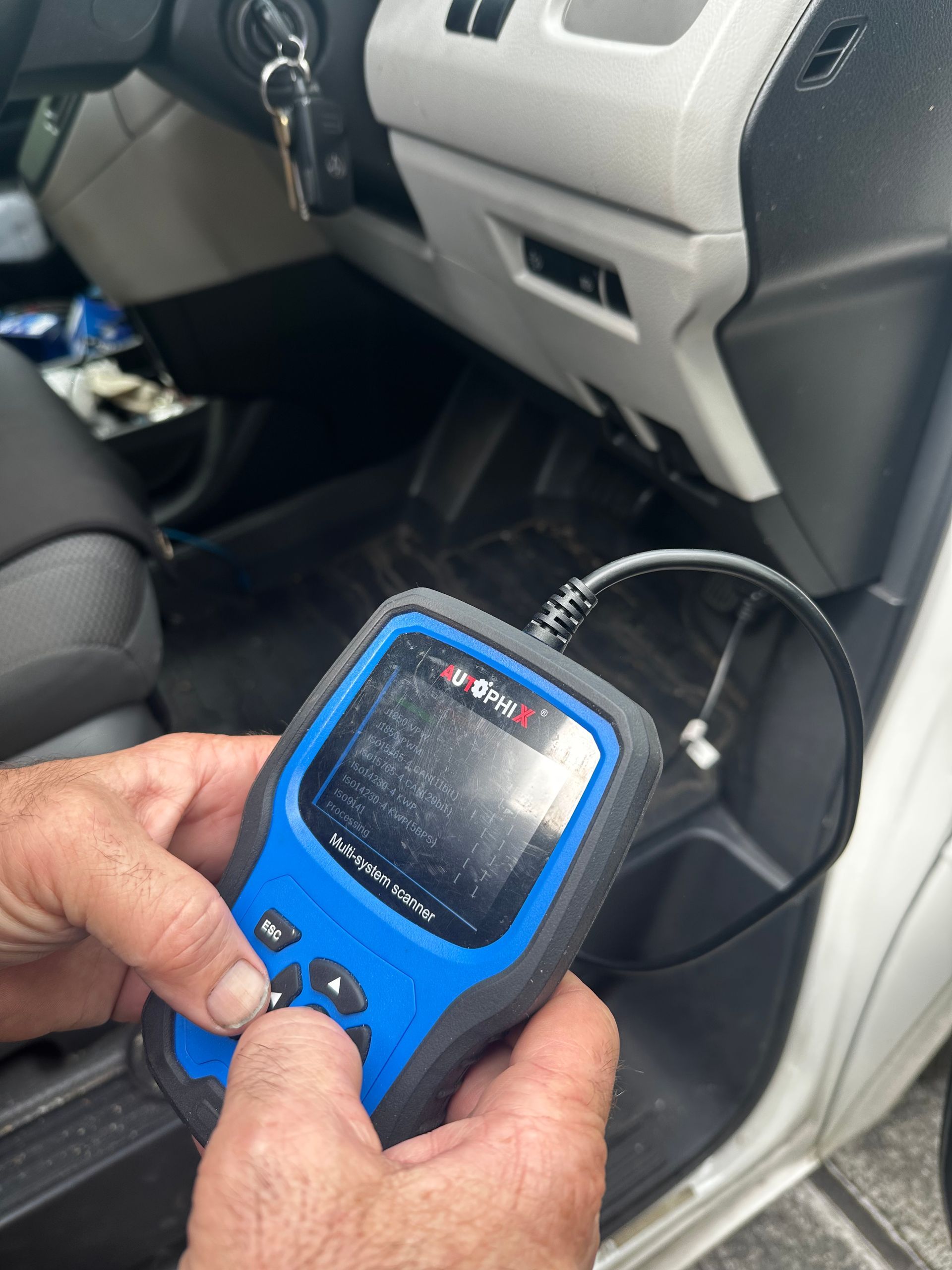 Hand holding a blue car diagnostic scanner inside a vehicle’s footwell near the dashboard. — Calvin's Mobile Mechanics In Currumbin, QLD