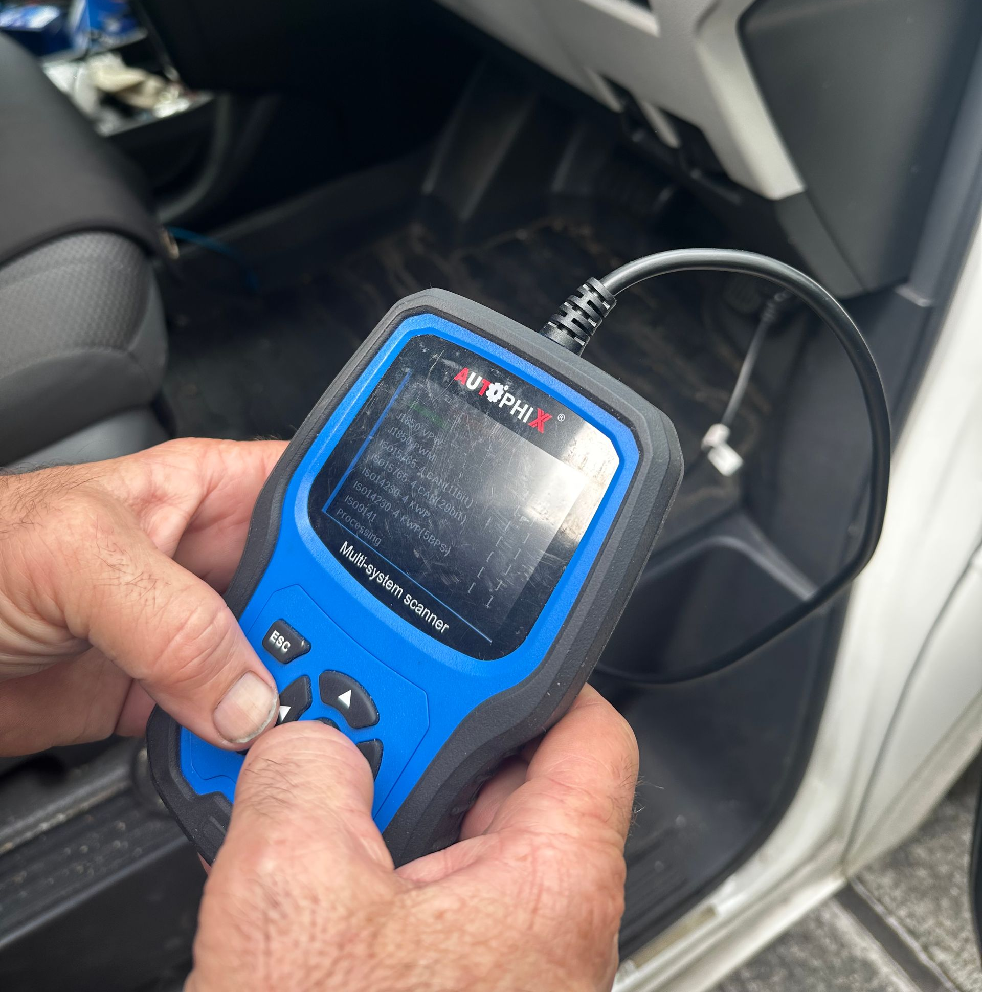 Hand holding a blue diagnostic device inside a car’s front passenger area  — Calvin's Mobile Mechanics In Elanora, QLD