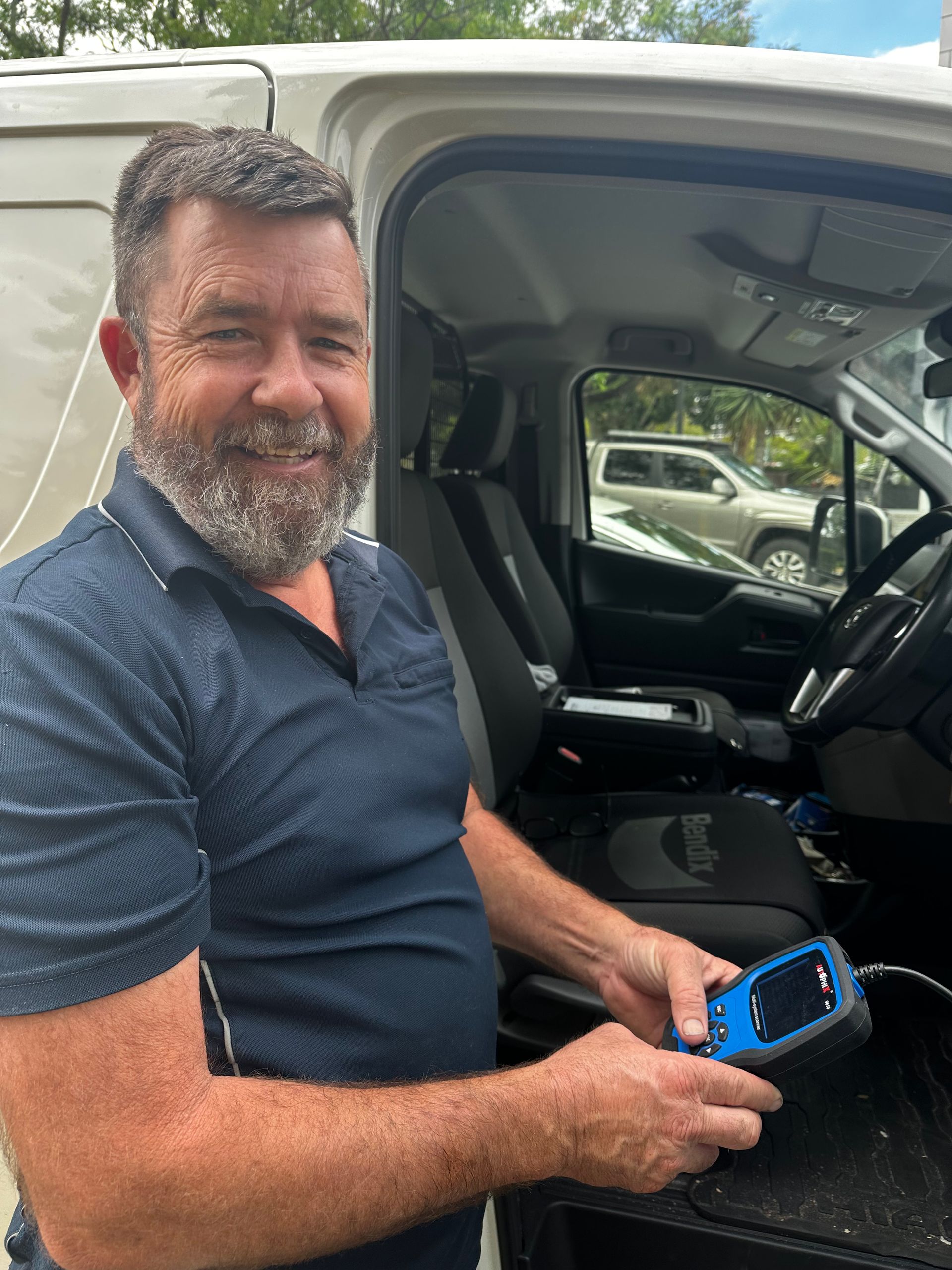 Man sitting in a pickup truck cabin, holding a blue device and smiling outdoors. — Calvin's Mobile Mechanics In Elanora, QLD