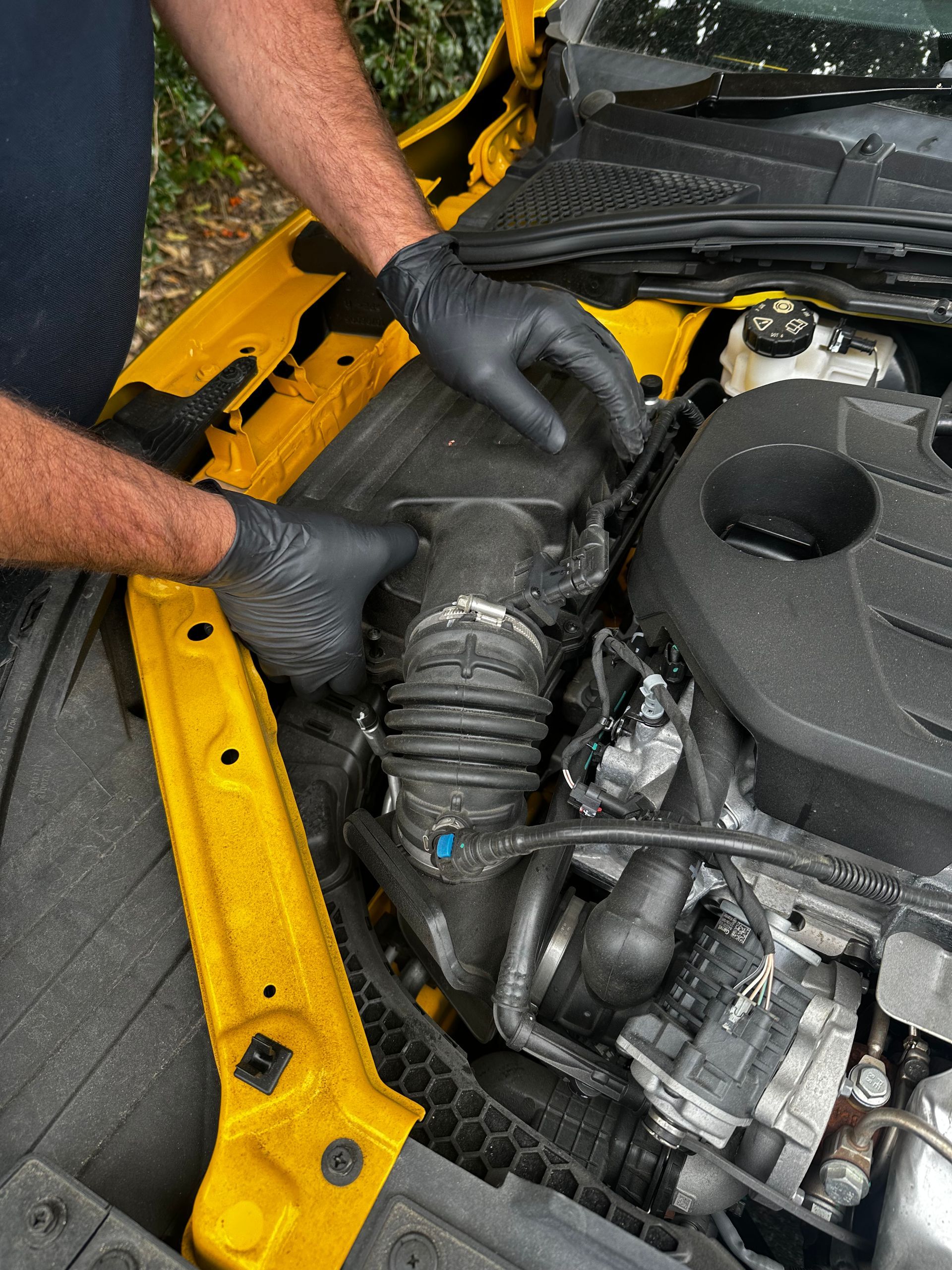 Gloved hands working on a car engine, inspecting a hose in the engine bay. — Calvin's Mobile Mechanics In Elanora, QLD