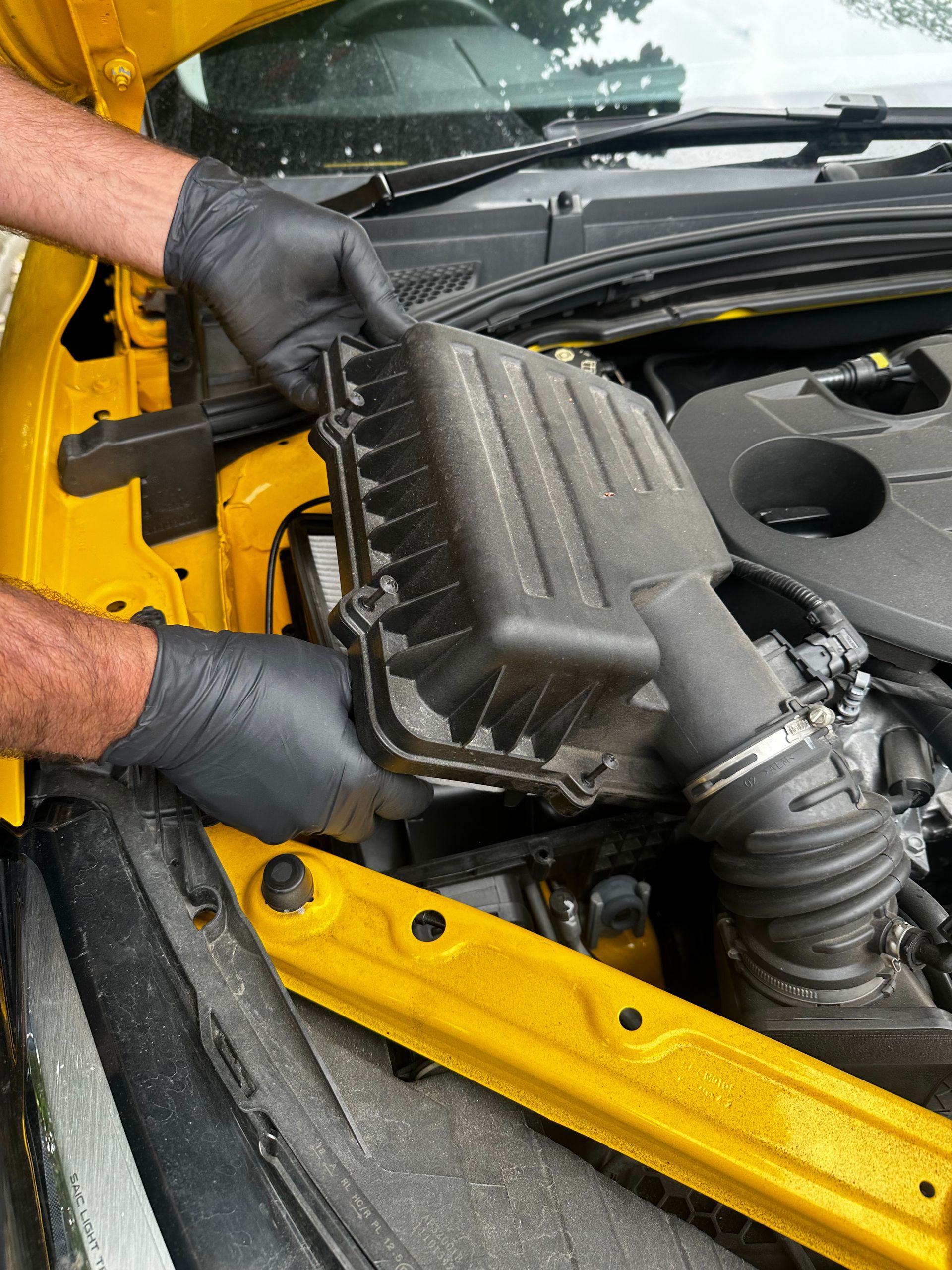 Gloved hands removing a black air filter box from a car engine bay. — Calvin's Mobile Mechanics In Upper Coomera, QLD