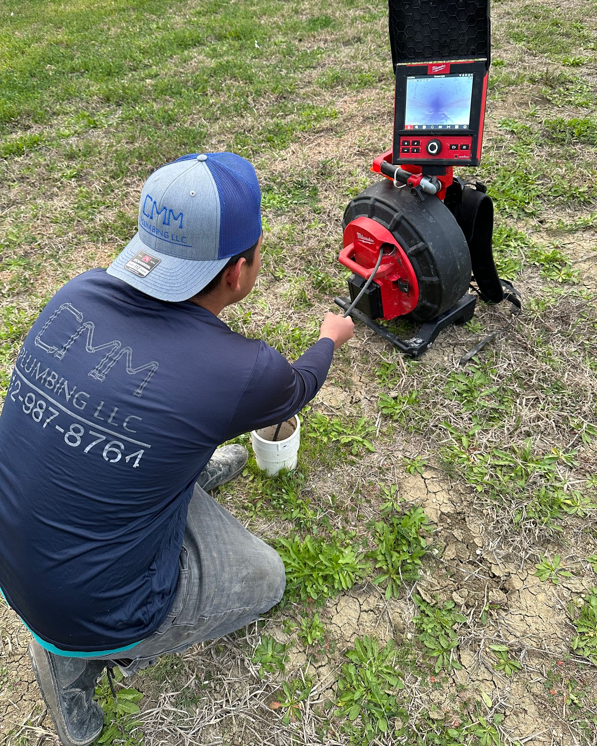 CMM plumber kneeling on grass performing camera inspection