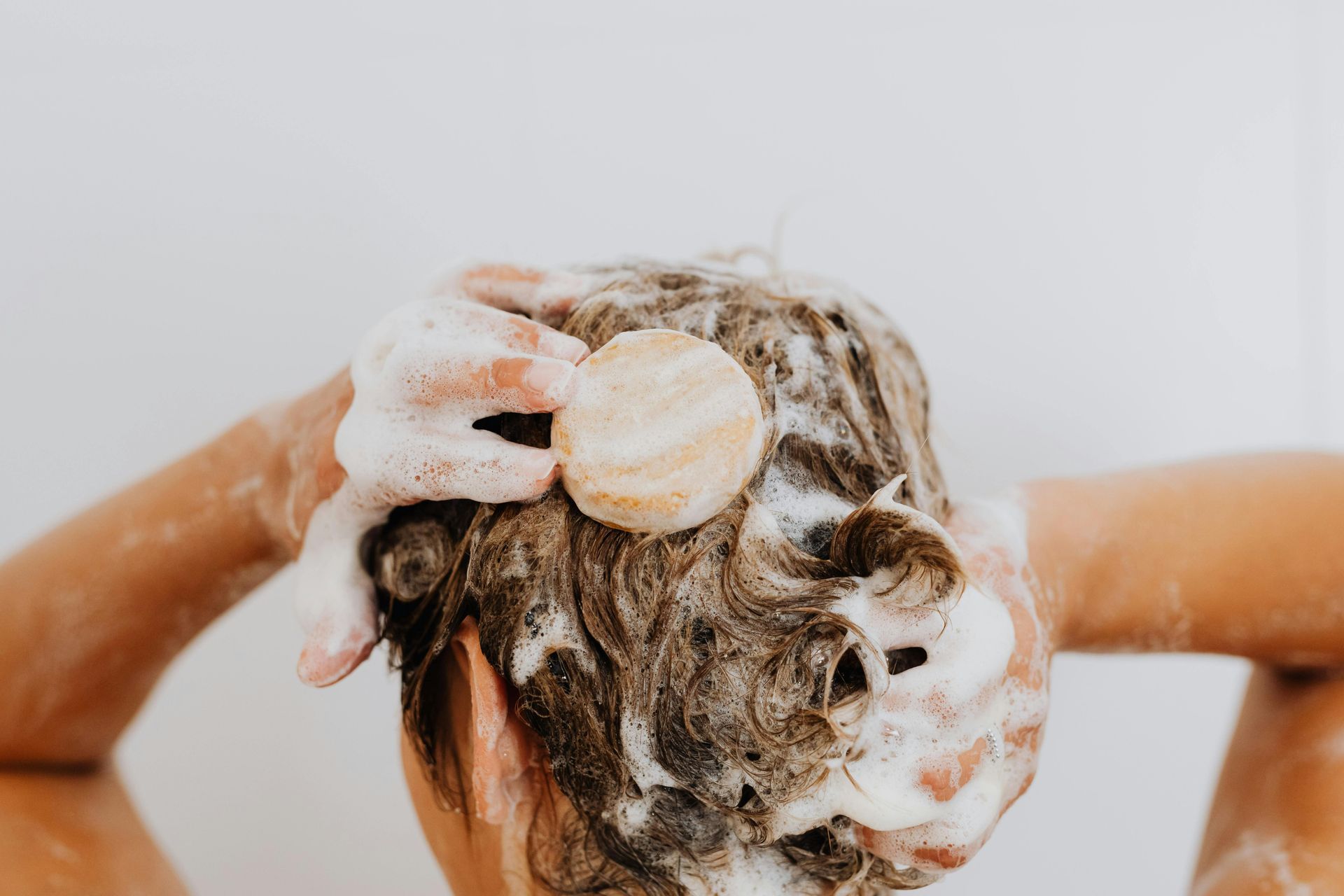 A woman is washing her hair in a bathtub with a wooden sponge causing for Hair and Soap Scum