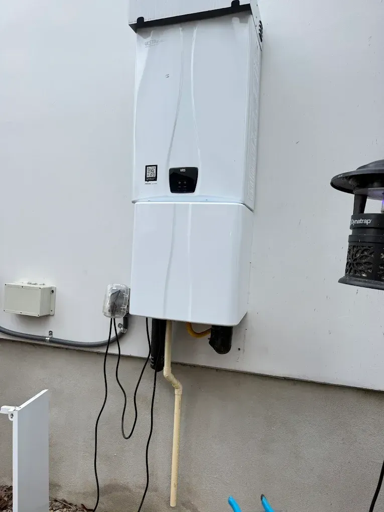 Wall-mounted tankless water heater on an exterior white building wall.