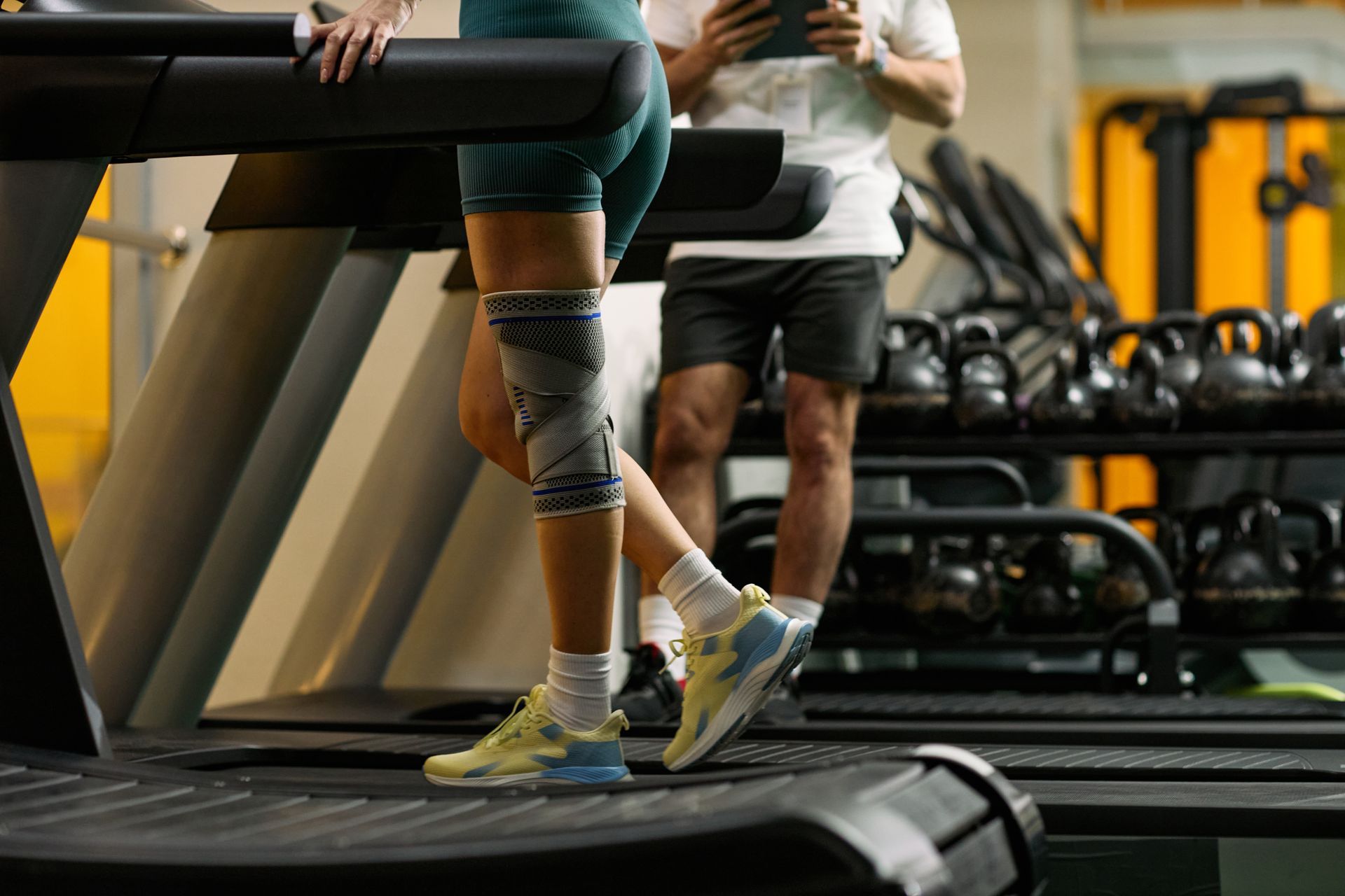 Woman wearing knee brace support walking on treadmill during gym workout rehabilitation. Woman wearing knee brace support walking on treadmill during gym workout rehabilitation.