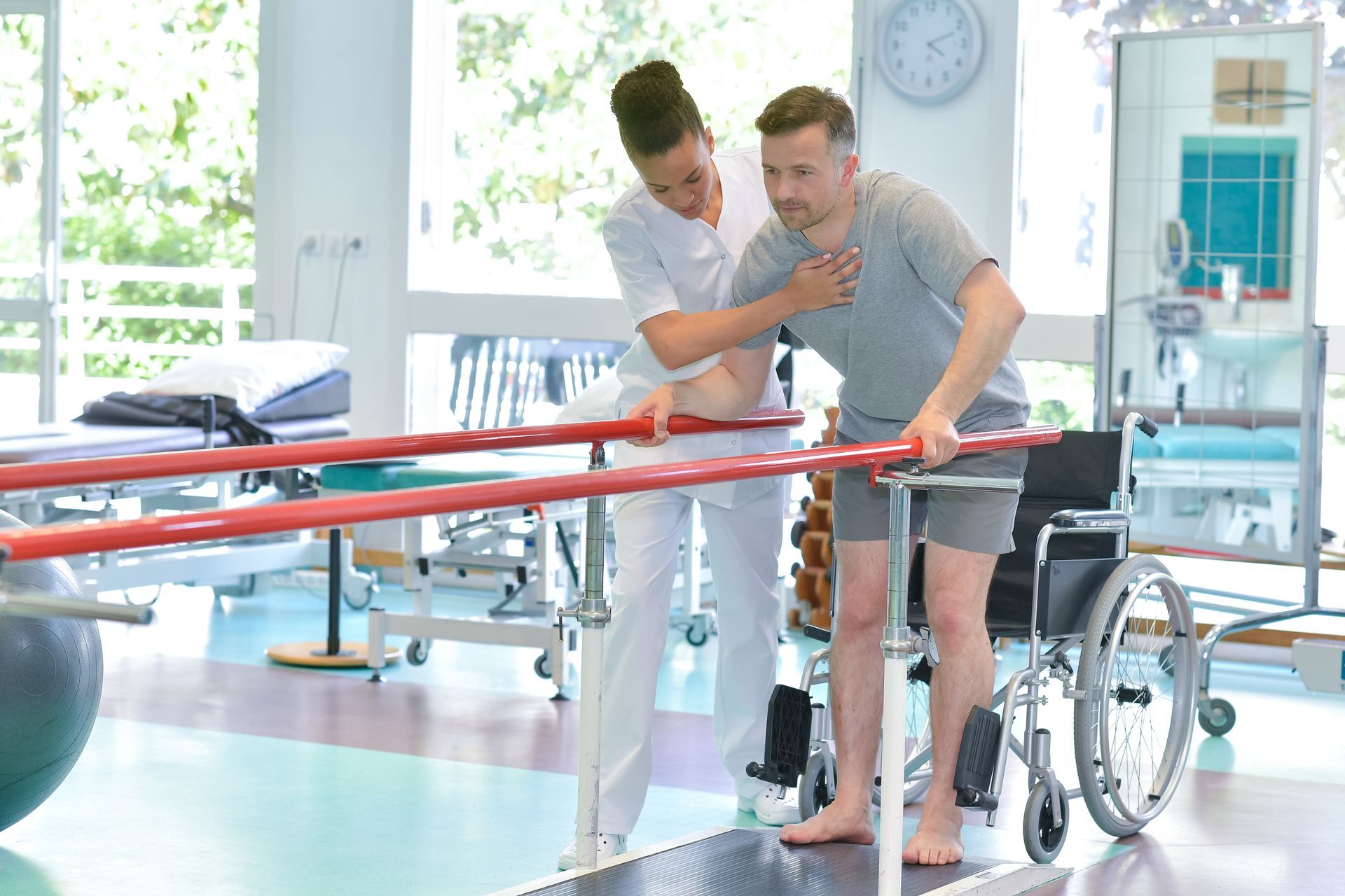 Therapist helping a patient walk between parallel bars at a rehab center.