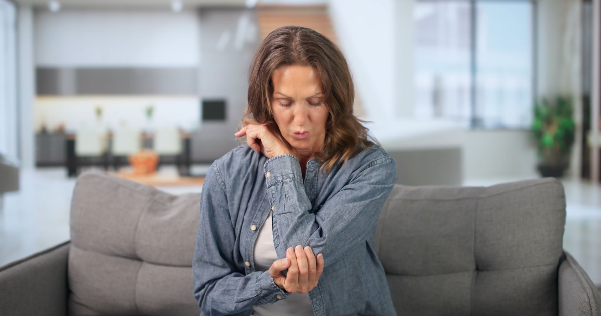 Woman on couch holding her wrist in pain before pain management treatment.