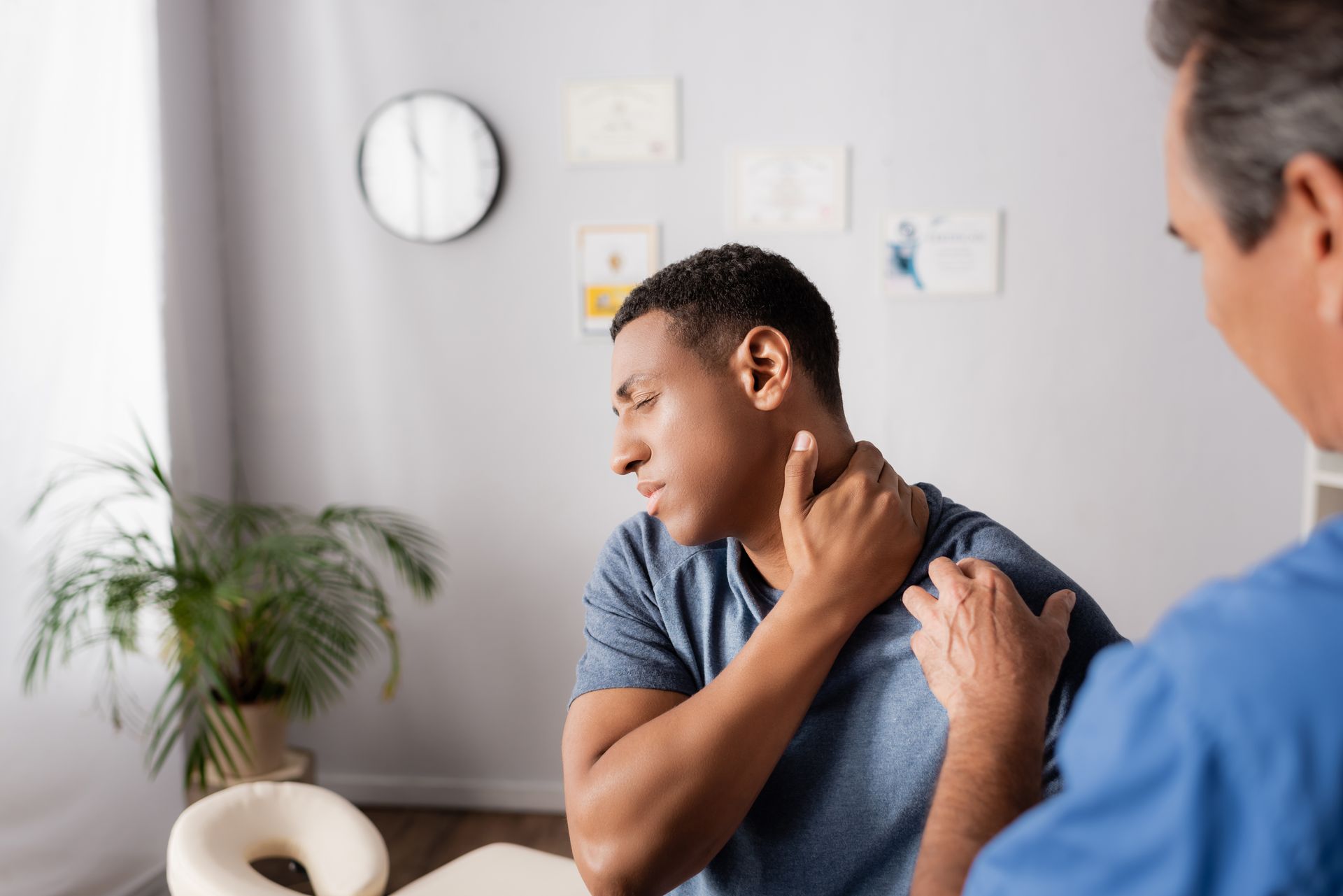 Person holding neck while clinician examines shoulder and neck in a medical office. Person holding neck while clinician examines shoulder and neck in a medical office.