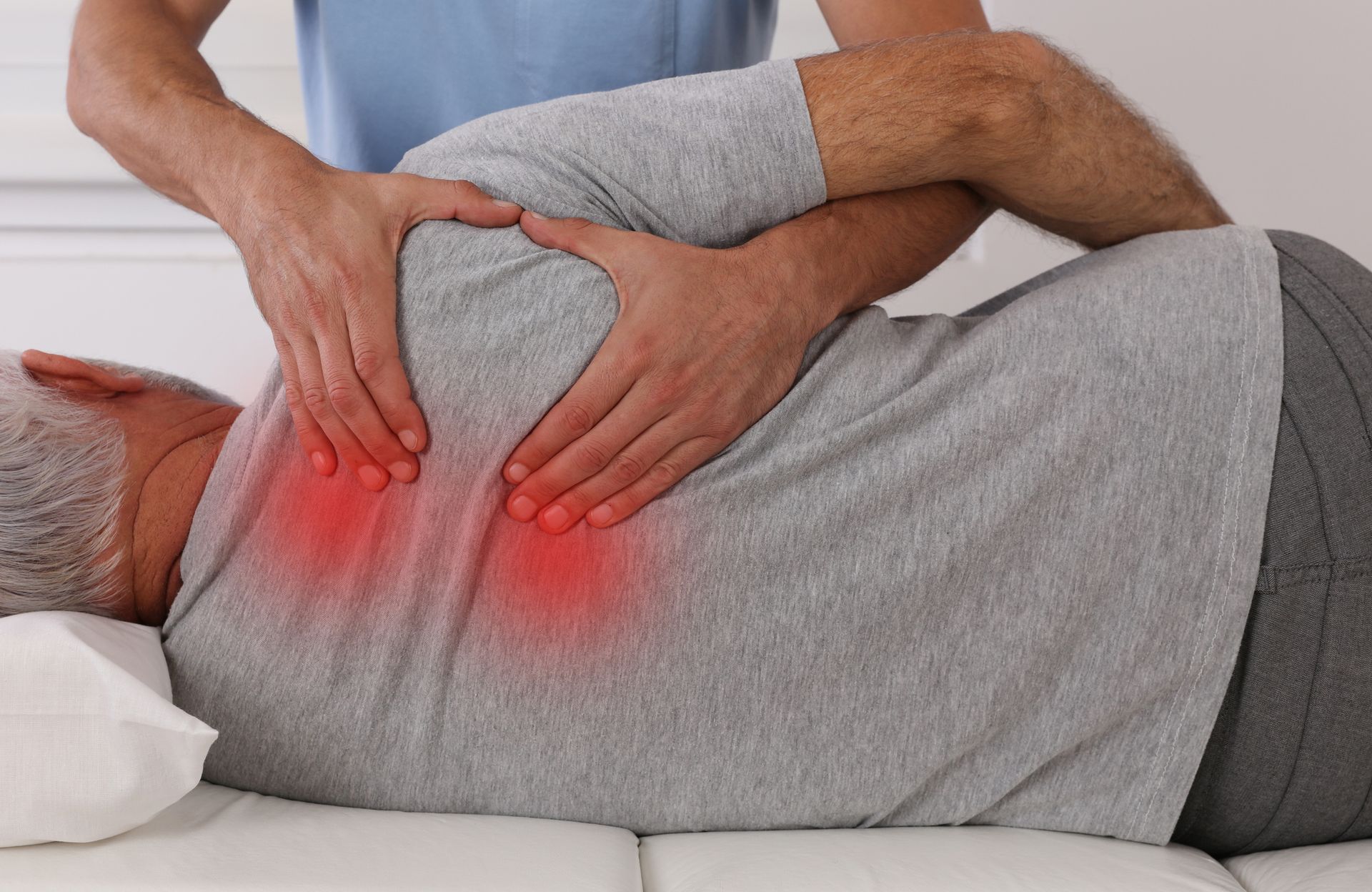 Man receiving a back massage on a white table; red areas highlight the painful spots.