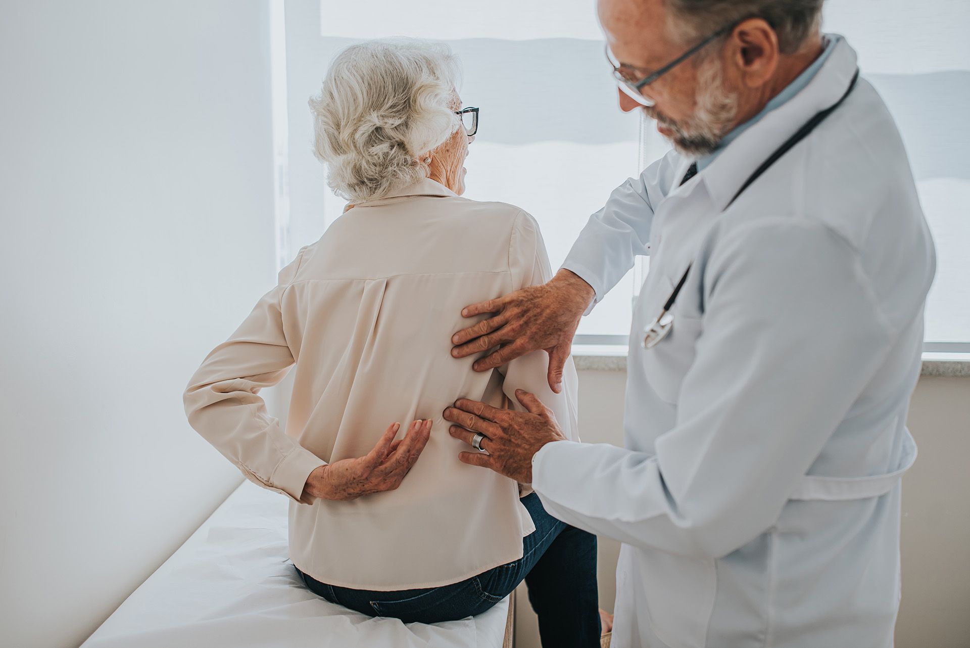 A senior patient with back pain is being treated by a pain management physician. Doctor examining a patient's back in a clinic setting.