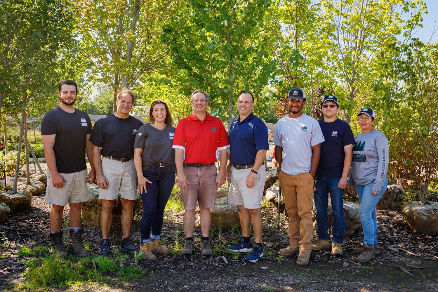Group of landscaping workers posing outdoors. They are standing in front of greenery.