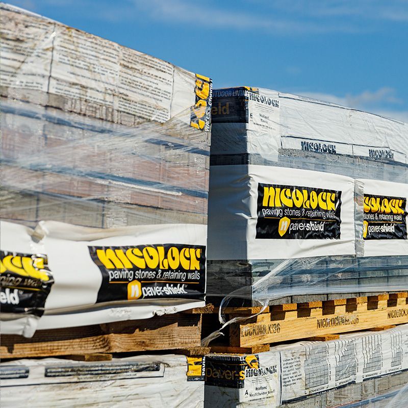 Pallets of NicLock paving stones, wrapped in plastic, stacked outdoors.
