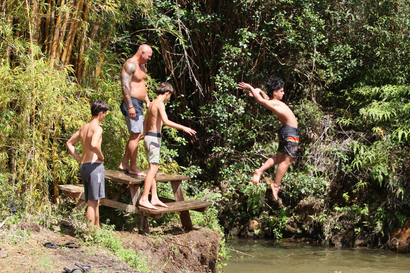 People jumping from a wooden platform into a river in a lush forest setting