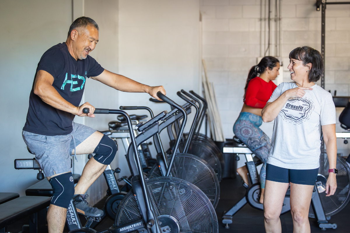 People exercising on treadmills and stationary bikes in a gym, with one person talking nearby