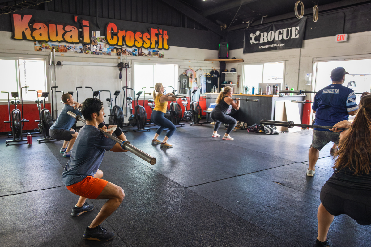 People doing squats in a CrossFit gym with kettlebells and workout equipment.