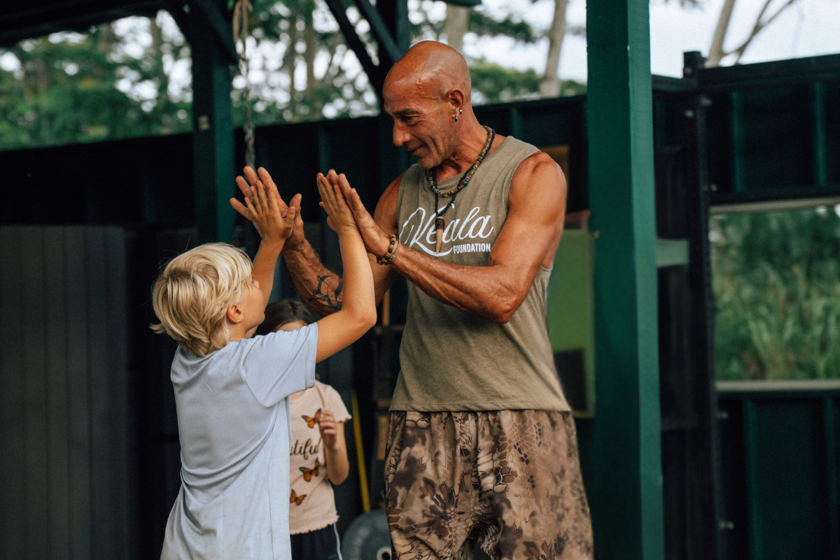 Two people high-five outdoors near a dark green building.