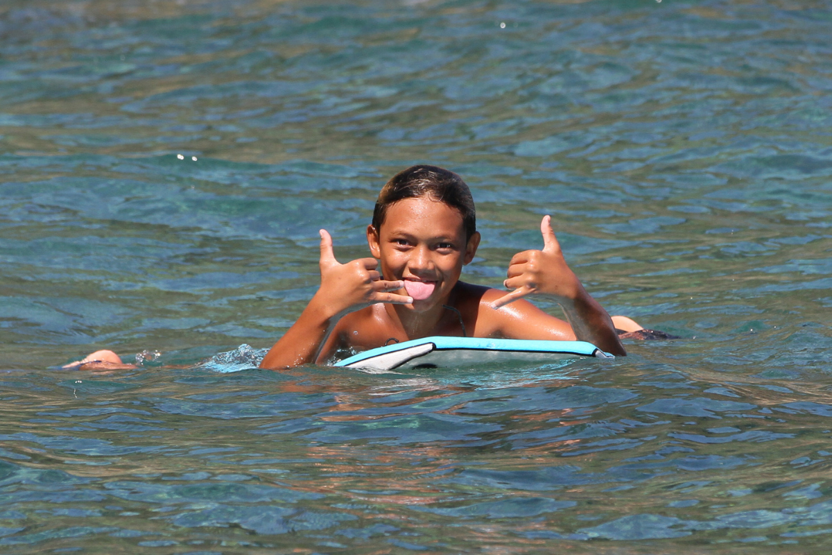 Smiling person in blue water giving two thumbs up while floating on a board
