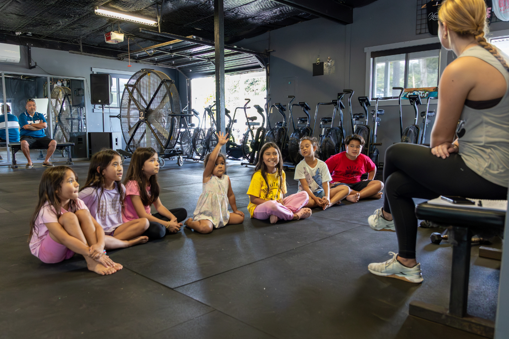 Children seated on a gym mat listening to an instructor in a fitness studio