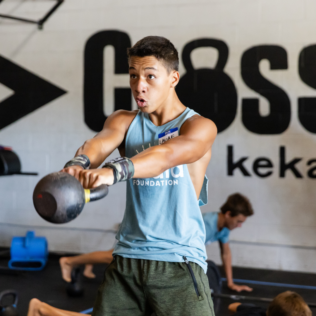 Person swinging a kettlebell in a gym, wearing a blue tank top and green shorts.