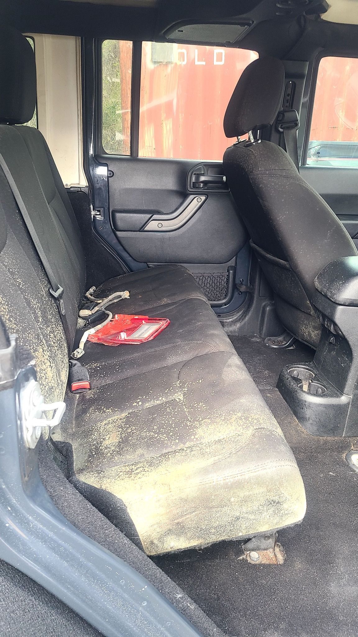 The back seat of a jeep is covered in dust and dirt.