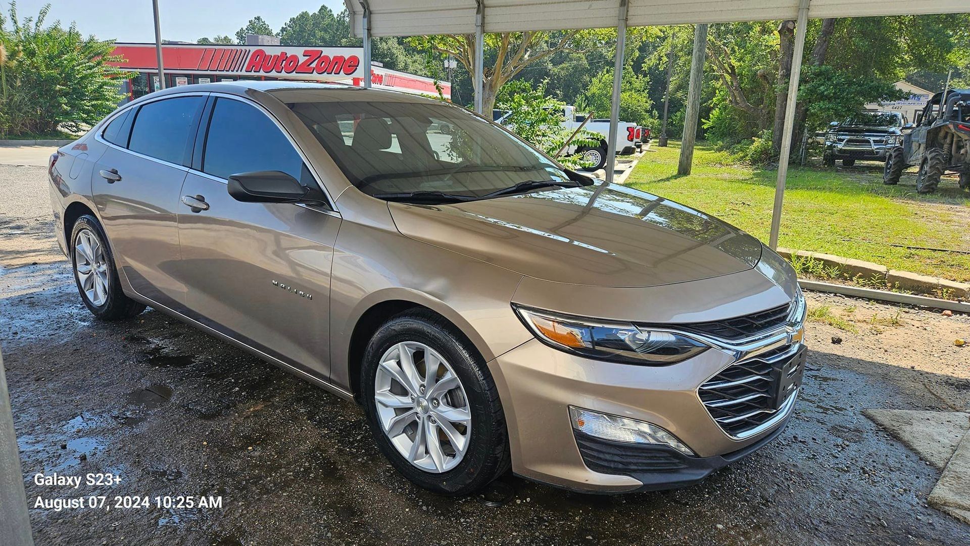 A brown chevrolet malibu is parked in front of a car wash.