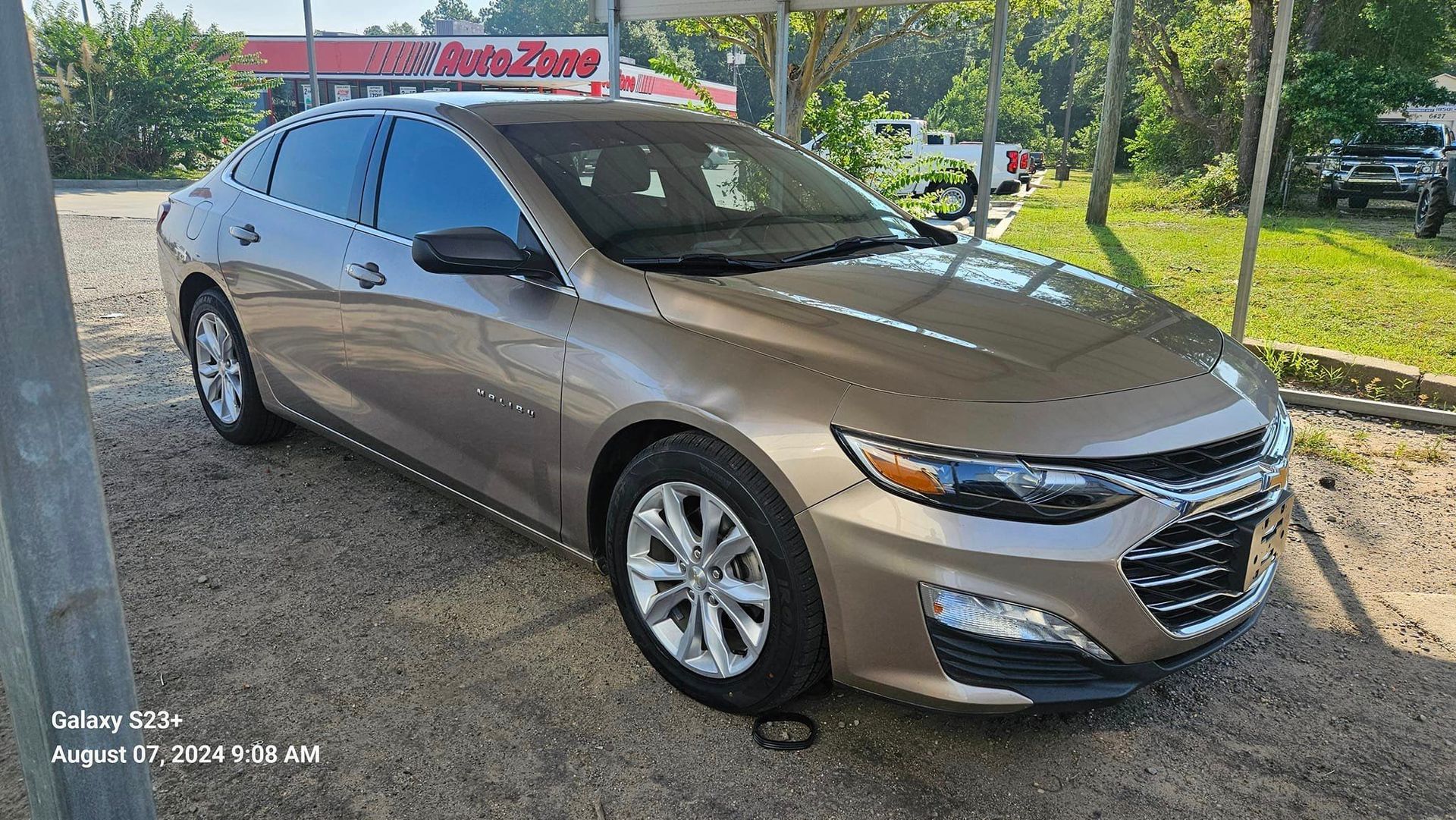 A brown chevrolet malibu is parked in a gravel lot.