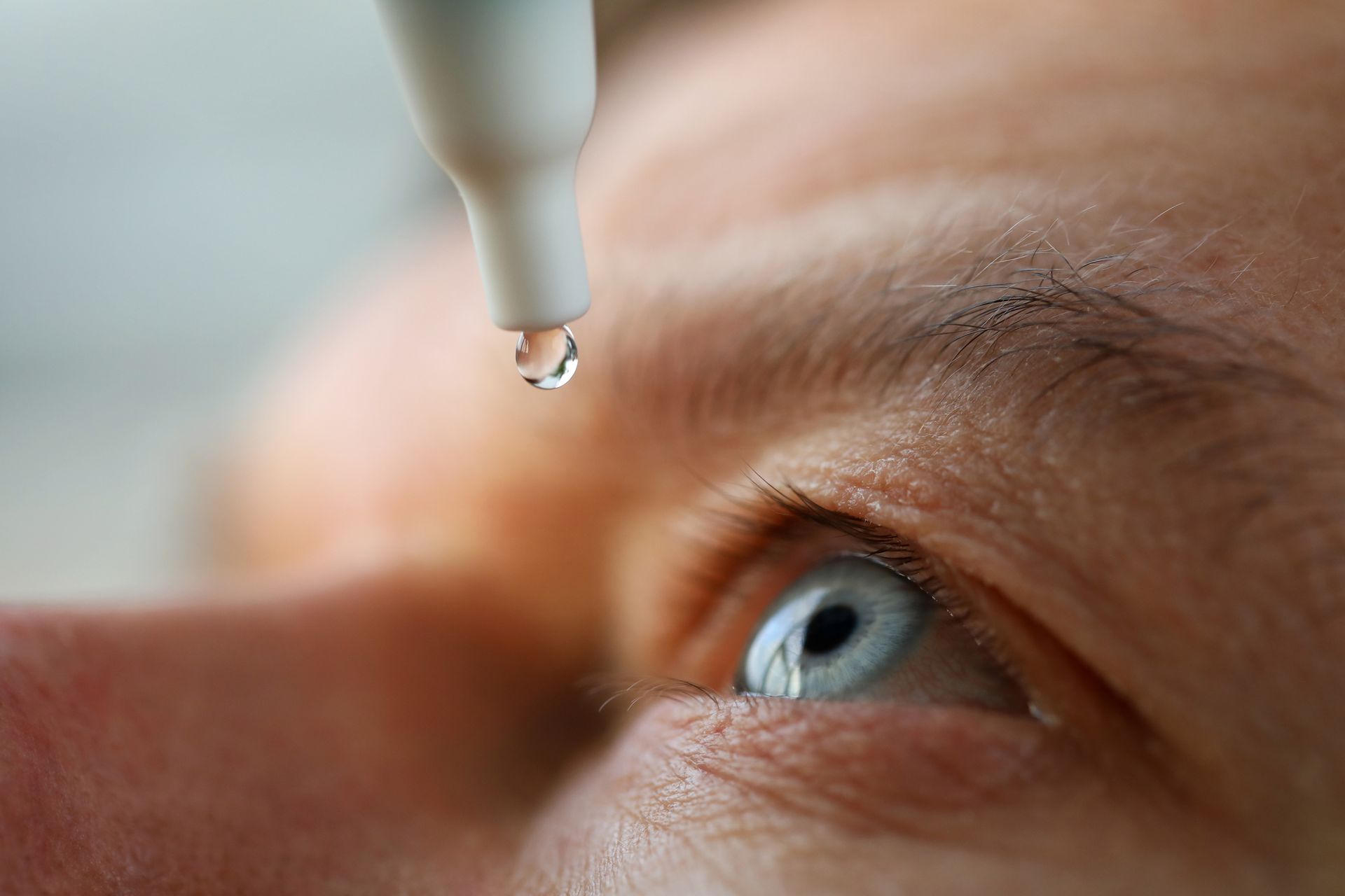 A close up of a person applying eye drops to their eye.