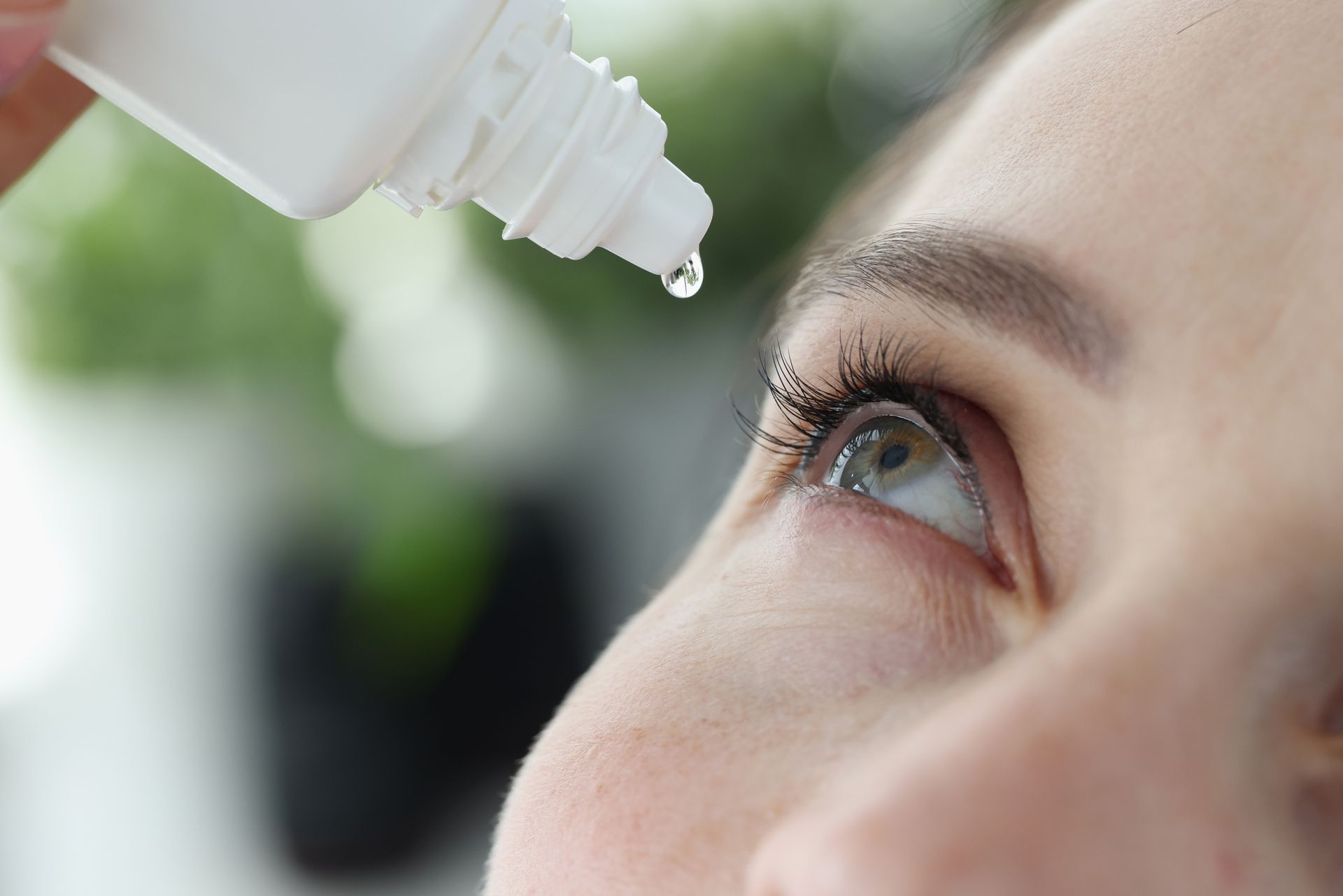 A woman is applying eye drops to her eye.