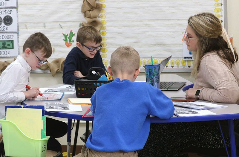 Three children and an adult at a table in a classroom, working. Extended Care | Immanuel Lutheran School | Belvidere, IL
