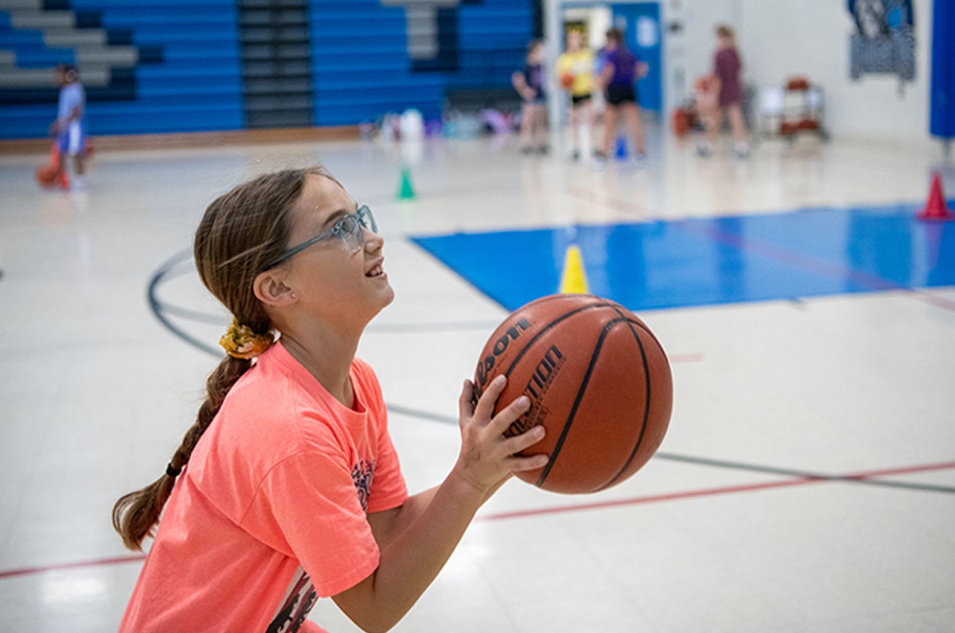 Girl in orange shirt with glasses holding a basketball. Elementary School | Immanuel Lutheran School | Belvidere, IL