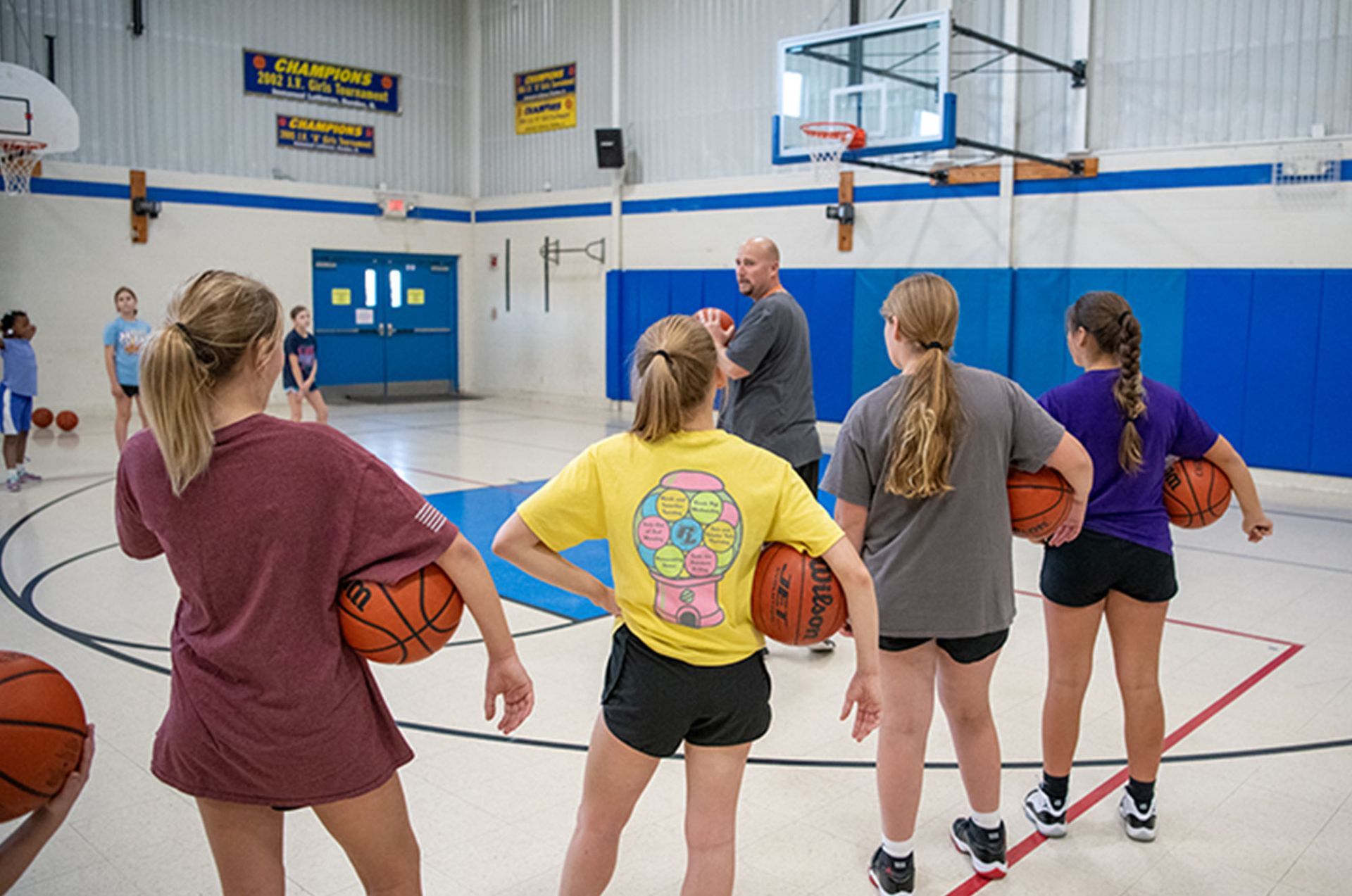 Basketball coach with young players on court, some holding balls. Middle School | Immanuel Lutheran School | Belvidere, IL