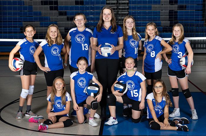 Youth volleyball team in blue uniforms posing in a gym. Coach holds volleyball.
