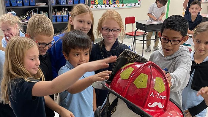 Children gathered around a red firefighter helmet, several touching it. Elementary School | Immanuel Lutheran School | Belvidere, IL