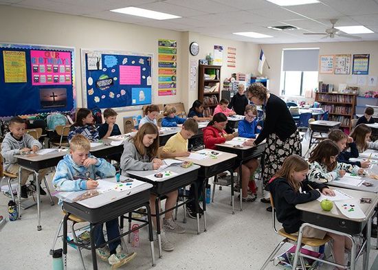 Students in desks at work, teacher assisting; classroom setting. Immanuel Lutheran School | Belvidere, IL