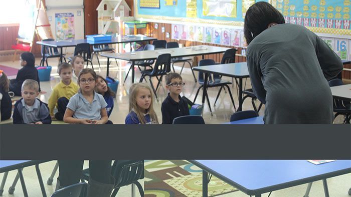 Children in a classroom listen to a teacher, some wearing glasses, seated at desks. Pre-K & Kindergarten | Immanuel Lutheran School | Belvidere, IL